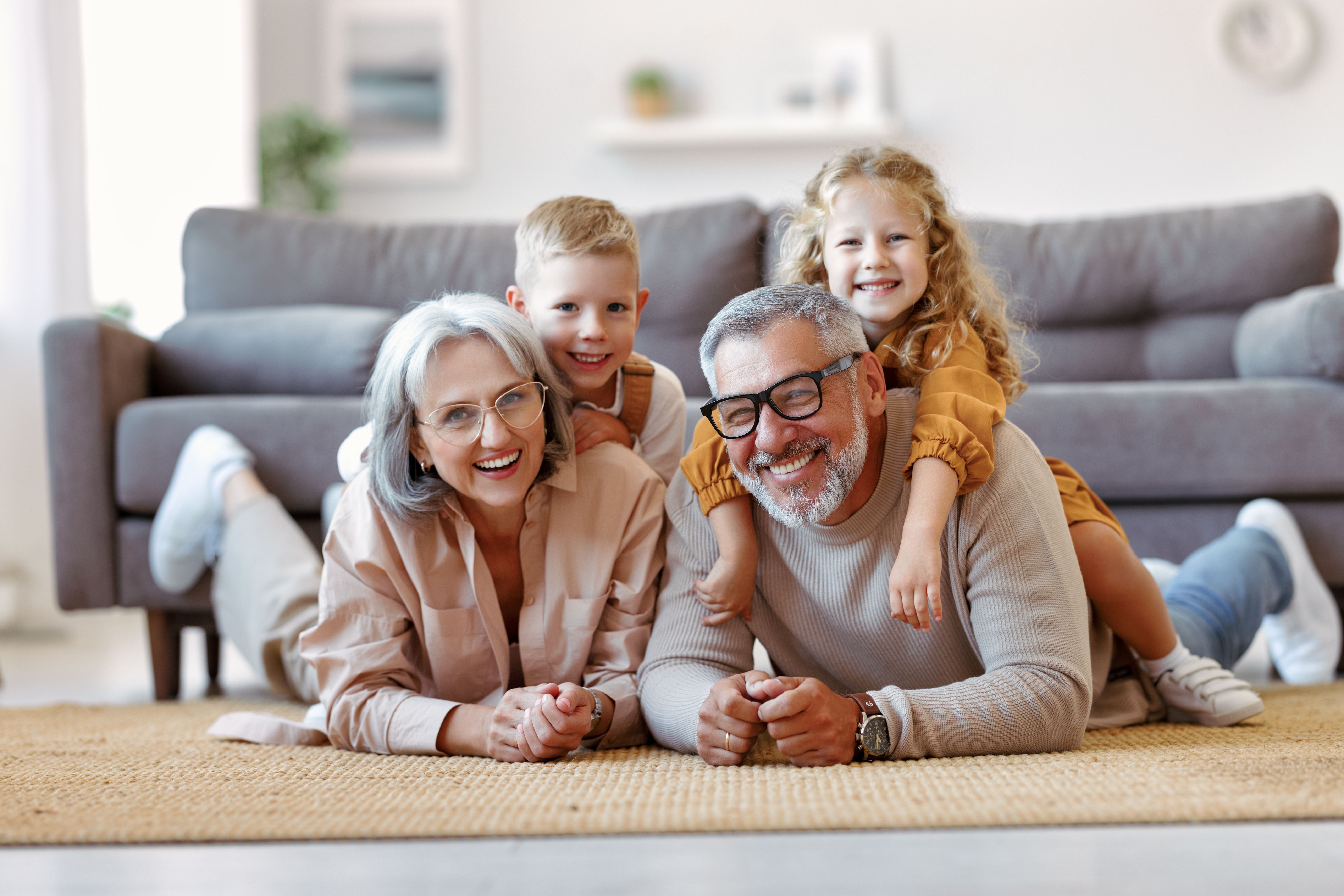 Beautiful cheerful family two cute little kids hugging with positive senior grandparents on floor