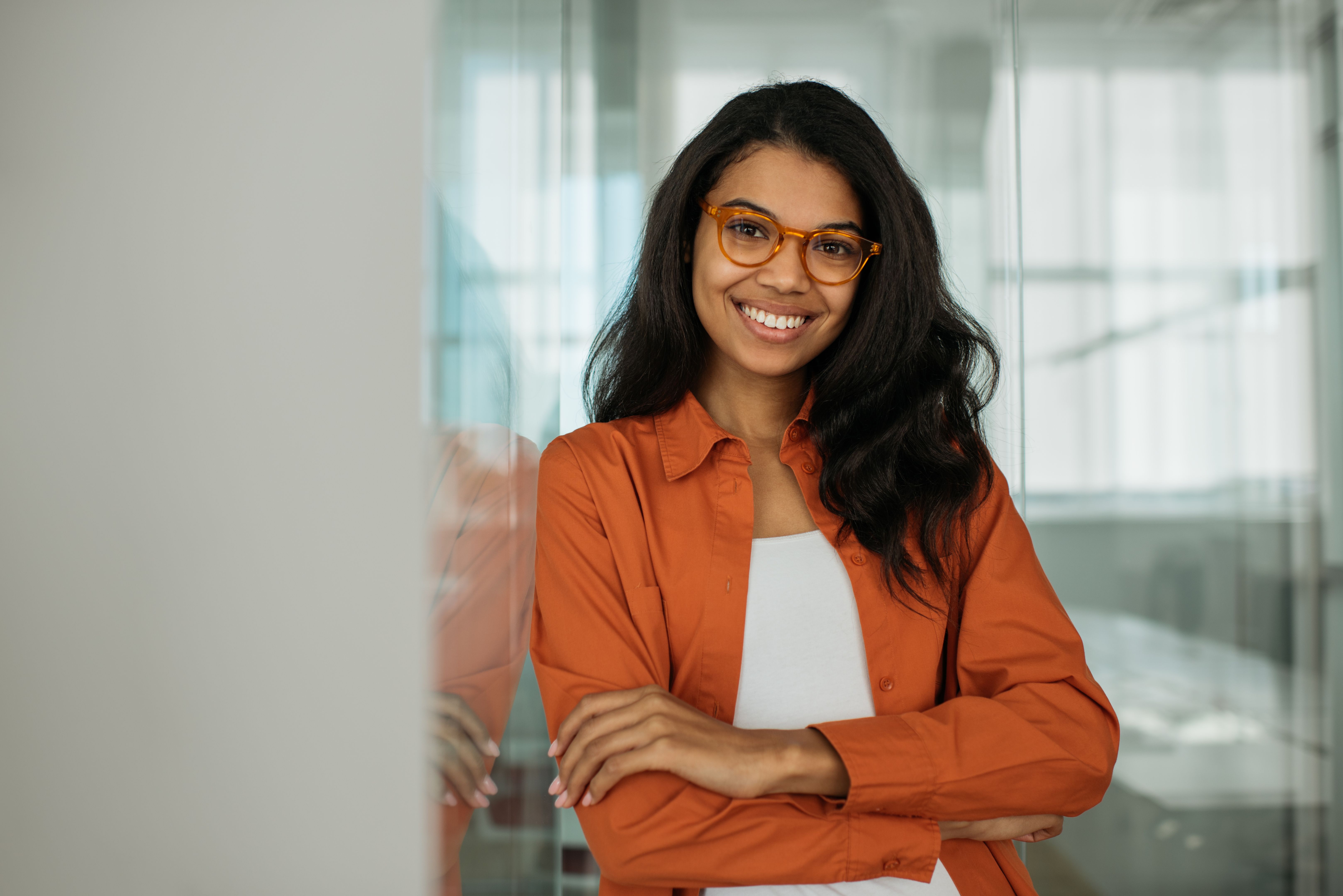 Smiling African American business woman wearing stylish eyeglasses looking at camera standing in modern office. Successful business and career concept Smiling African American business woman wearing stylish eyeglasses looking at camera standing in modern office. Successful business and career concept