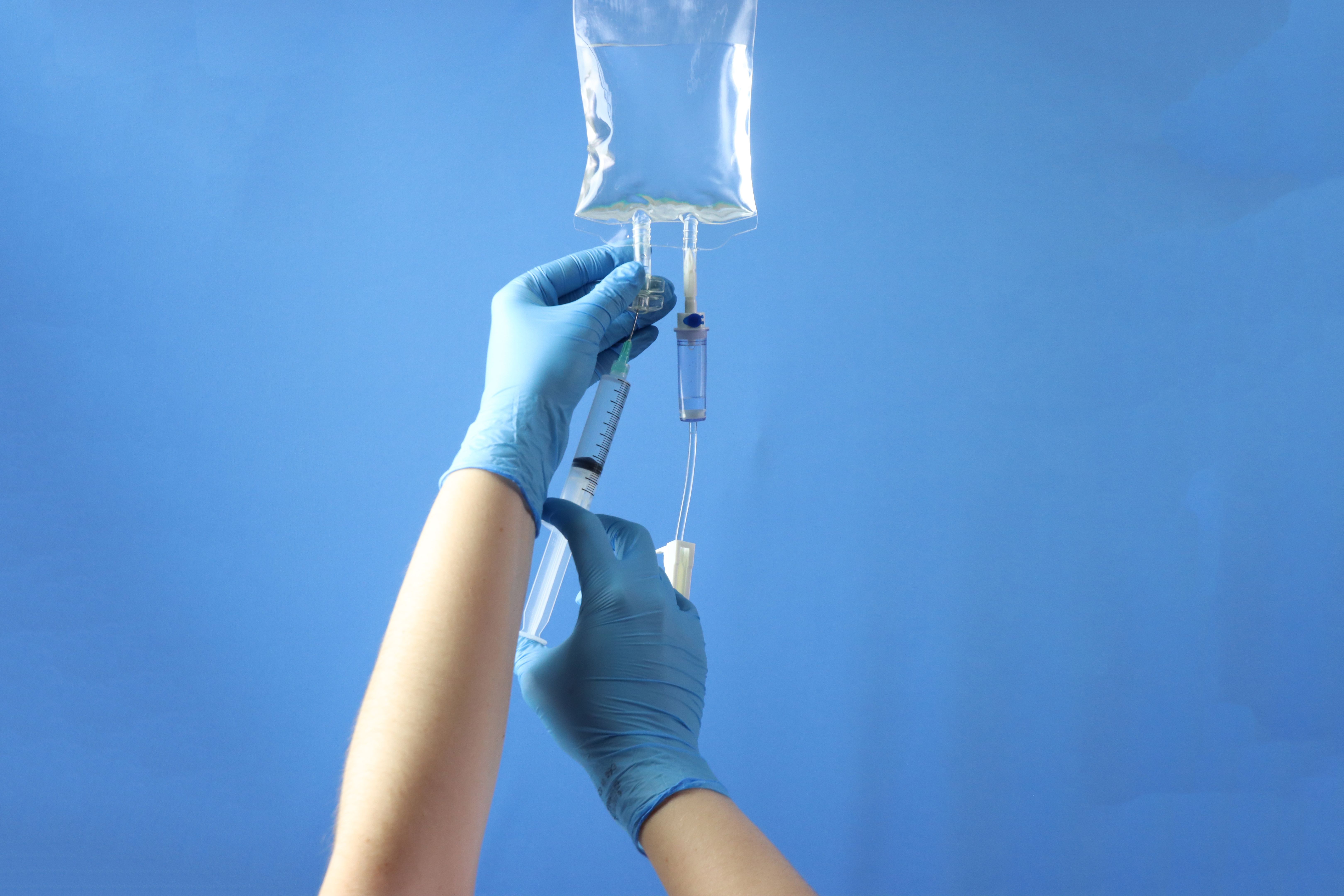 Drug bag with a infusion set connected to delivery the drug to the pacient. Professional holding the bag to infuse the drug with a syringe