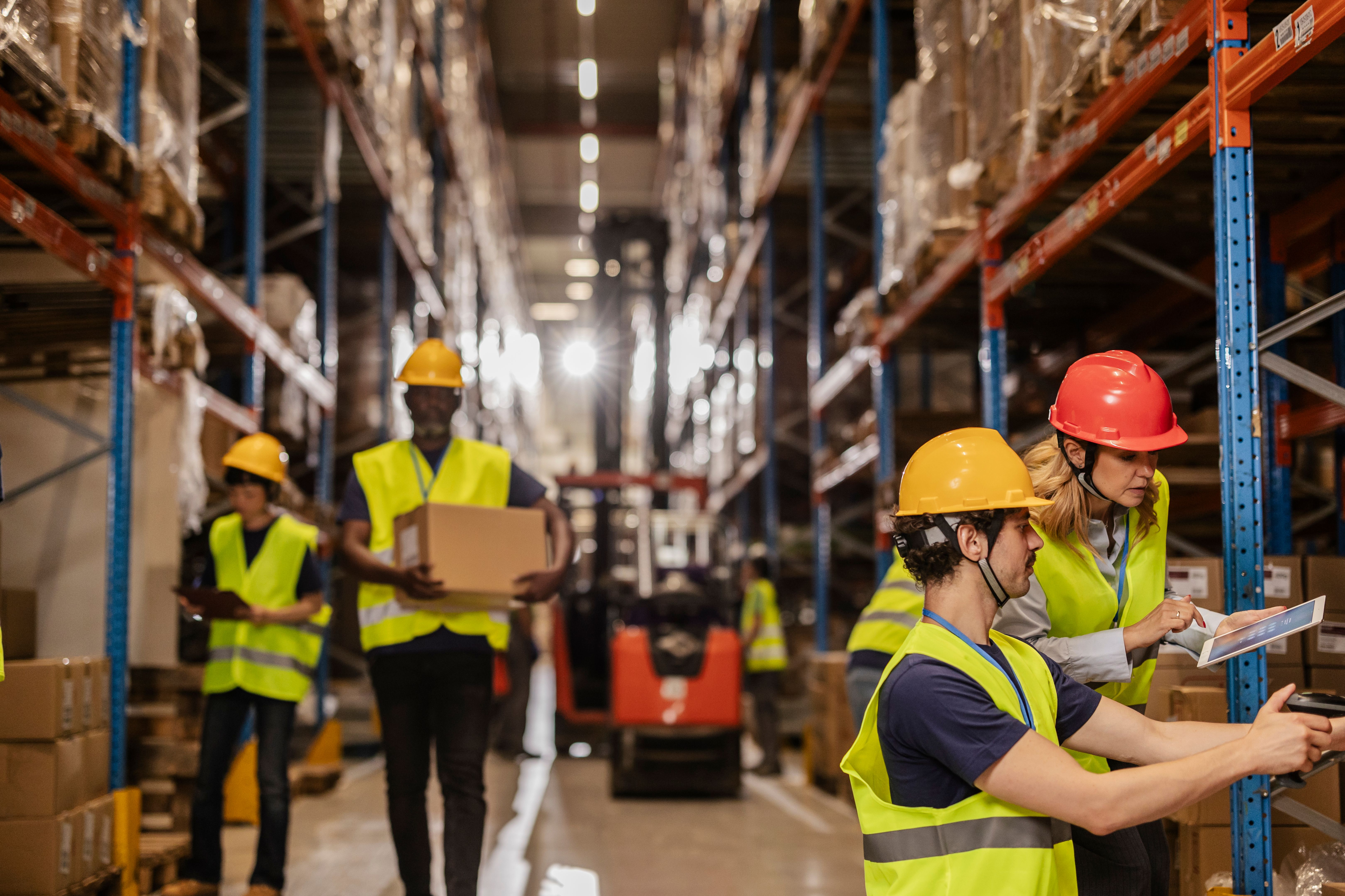Warehouse workers managing inventory with digital tablet and carrying boxes
