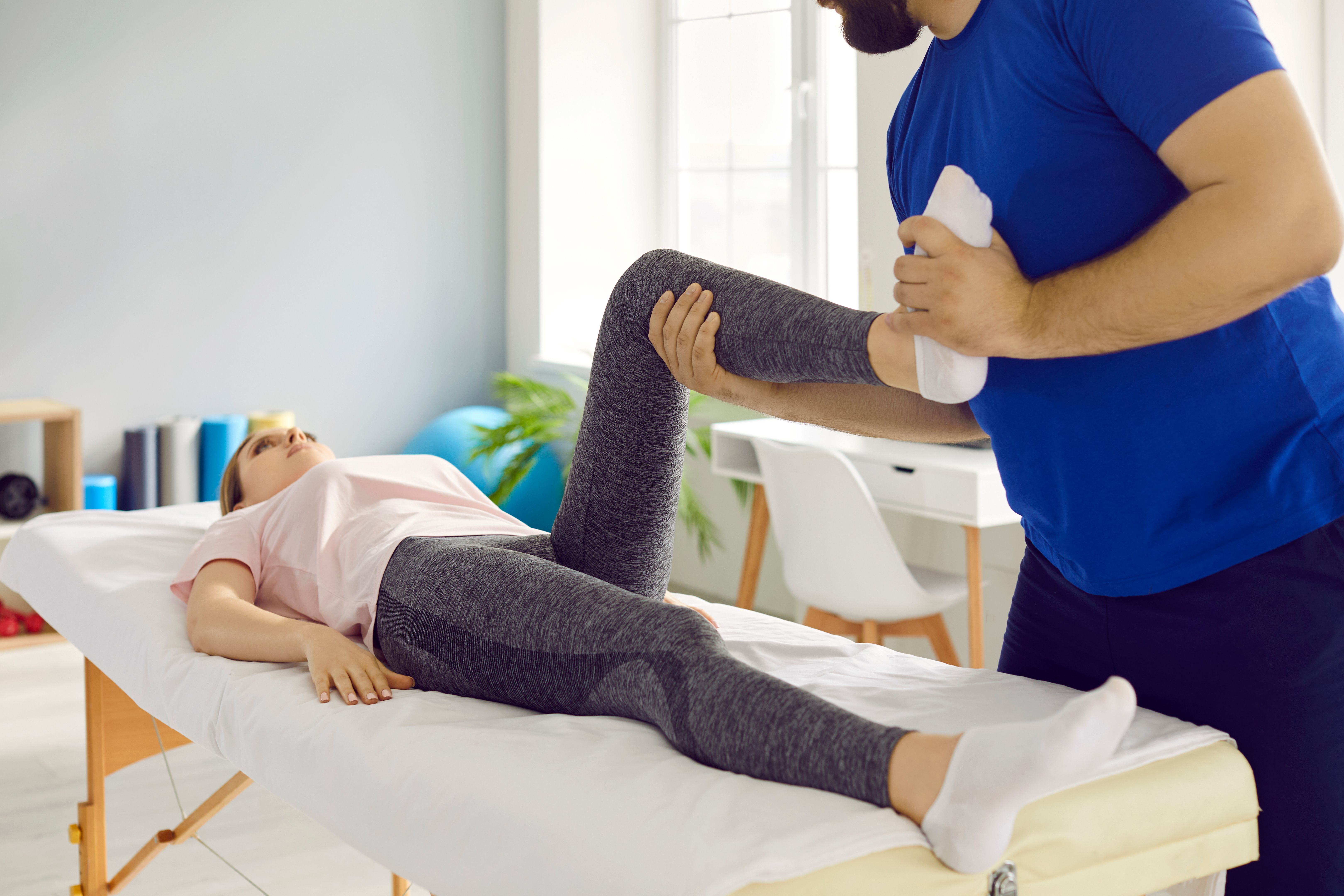 Professional physiotherapist at modern clinic examining knee flexion of young woman