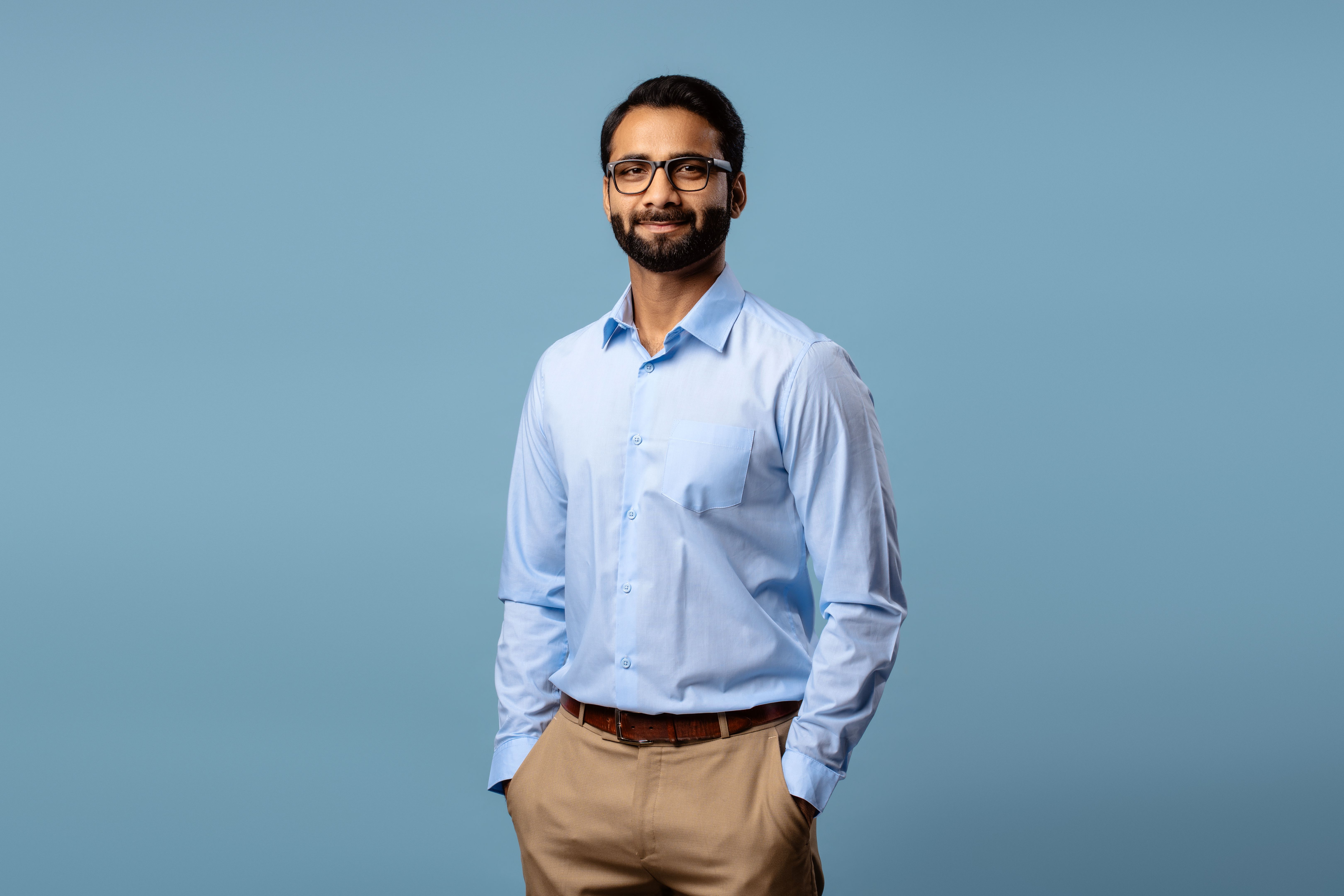 Portrait of confident Indian businessman wearing eyeglasses, hands in pockets, looking at camera