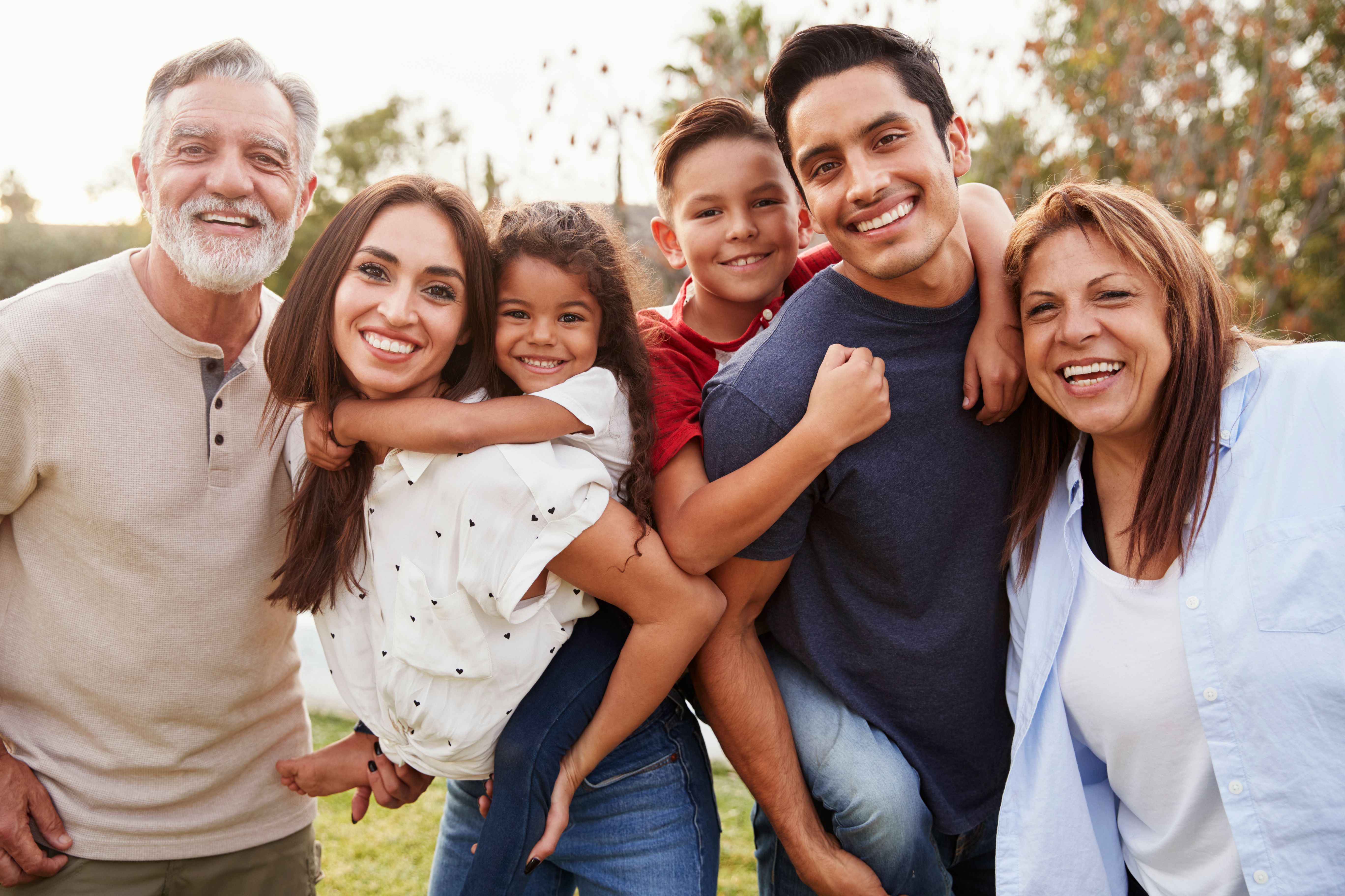 Three generation Hispanic family standing in the park, smiling to camera, selective focus Three generation Hispanic family standing in the park, smiling to camera, selective focus