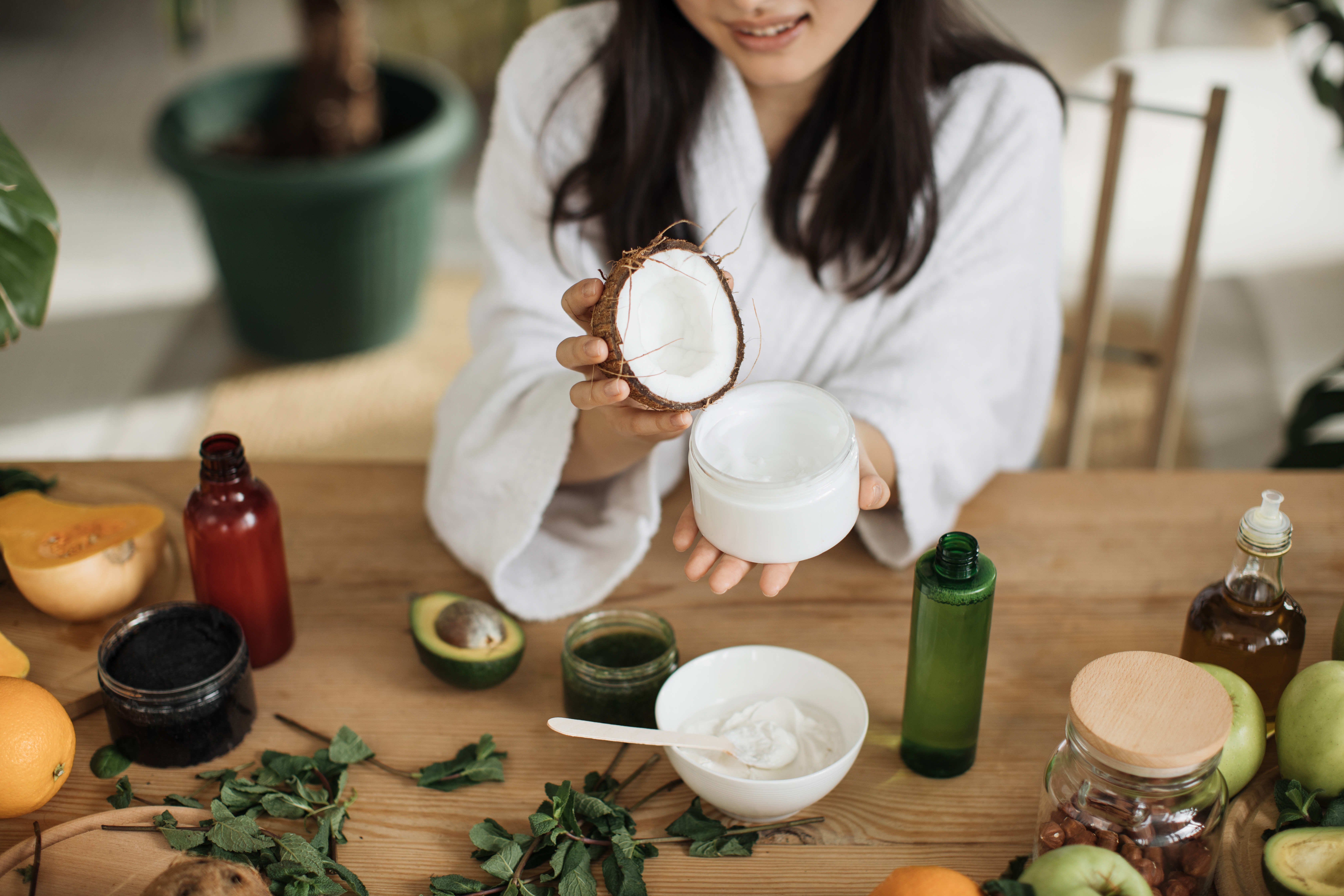 Close up hands of young woman holding half of coconut while making homemade cream for healthy skin Close up hands of young woman holding half of coconut while making homemade cream for healthy skin