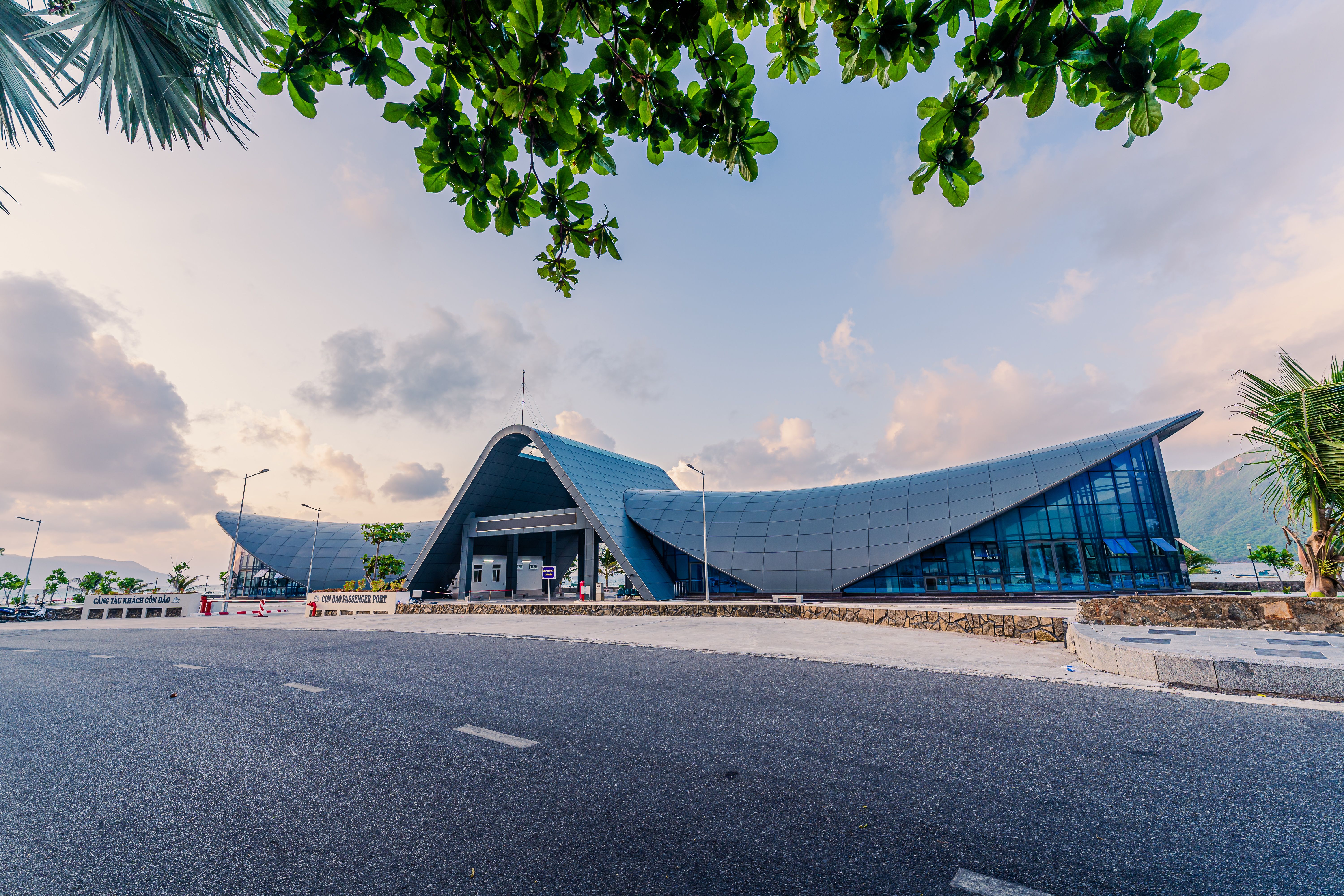 View of new Con Dao passenger port in Con Son town, a peaceful Con Dao island, Vietnam. Coastal view with waves, coastline, clear sky, blue sea, tourists and mountain.