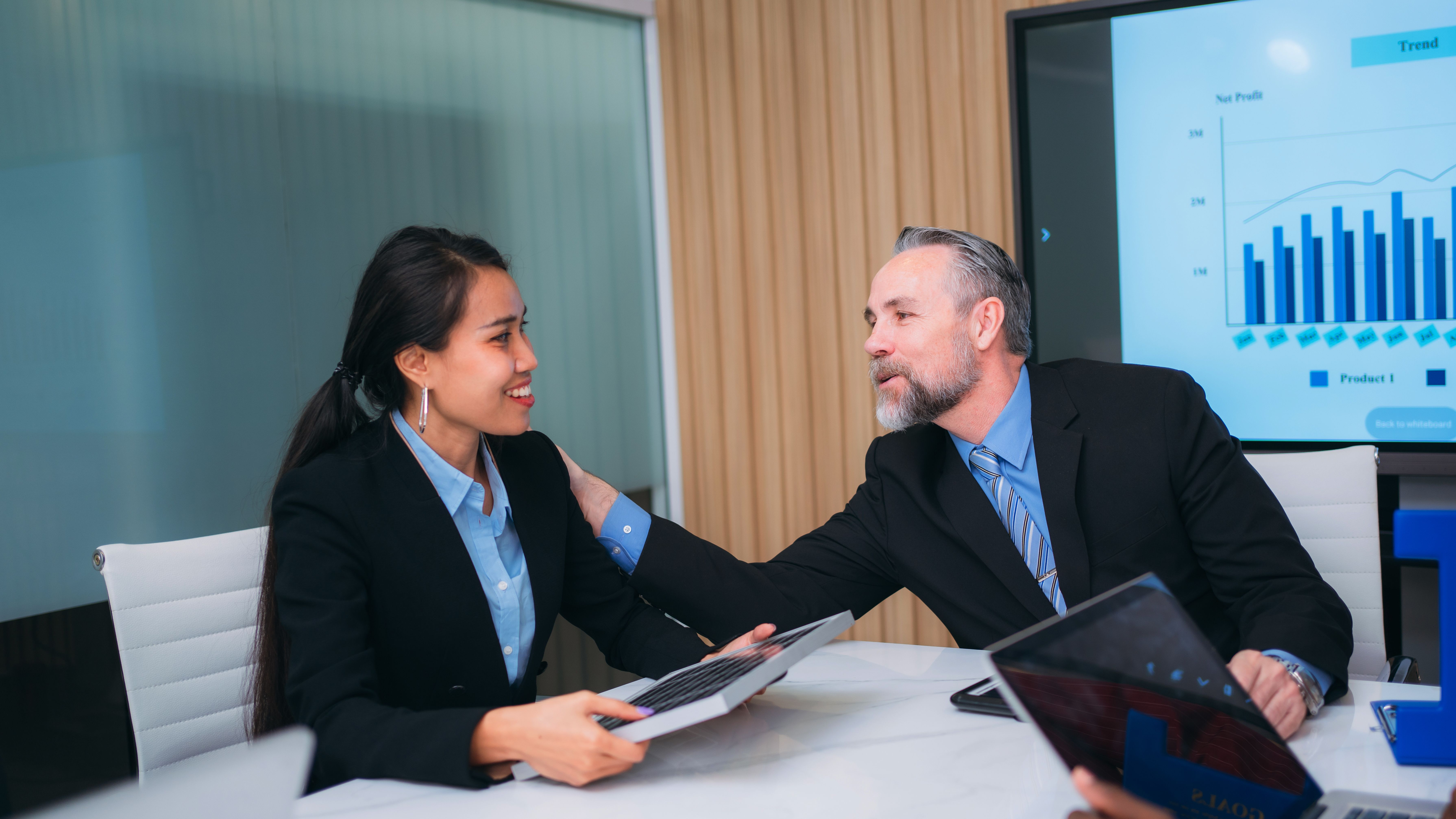 A group of different business people are sitting around a big meeting table in a modern office.
