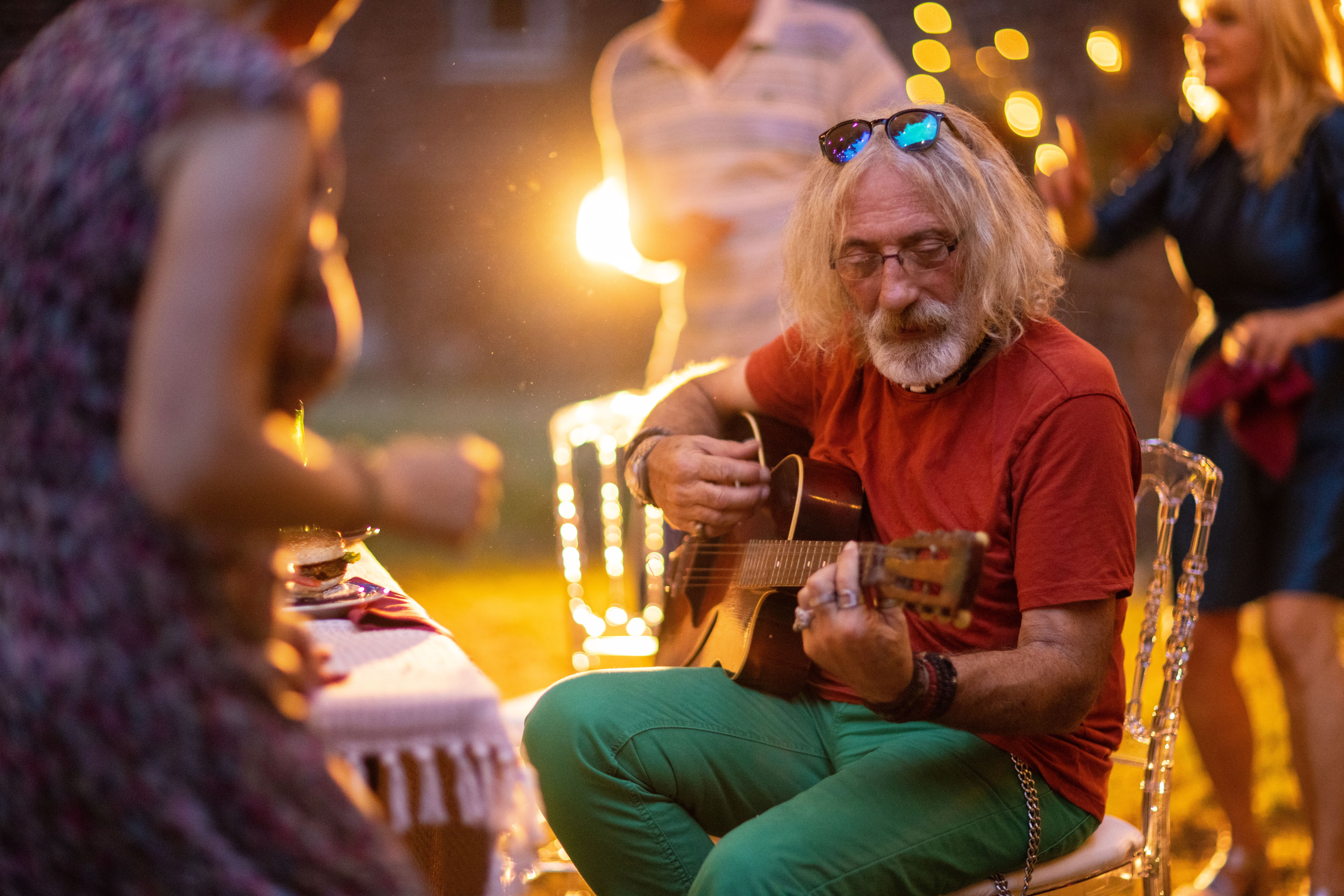 Senior man playing acoustic guitar for his friends on garden party