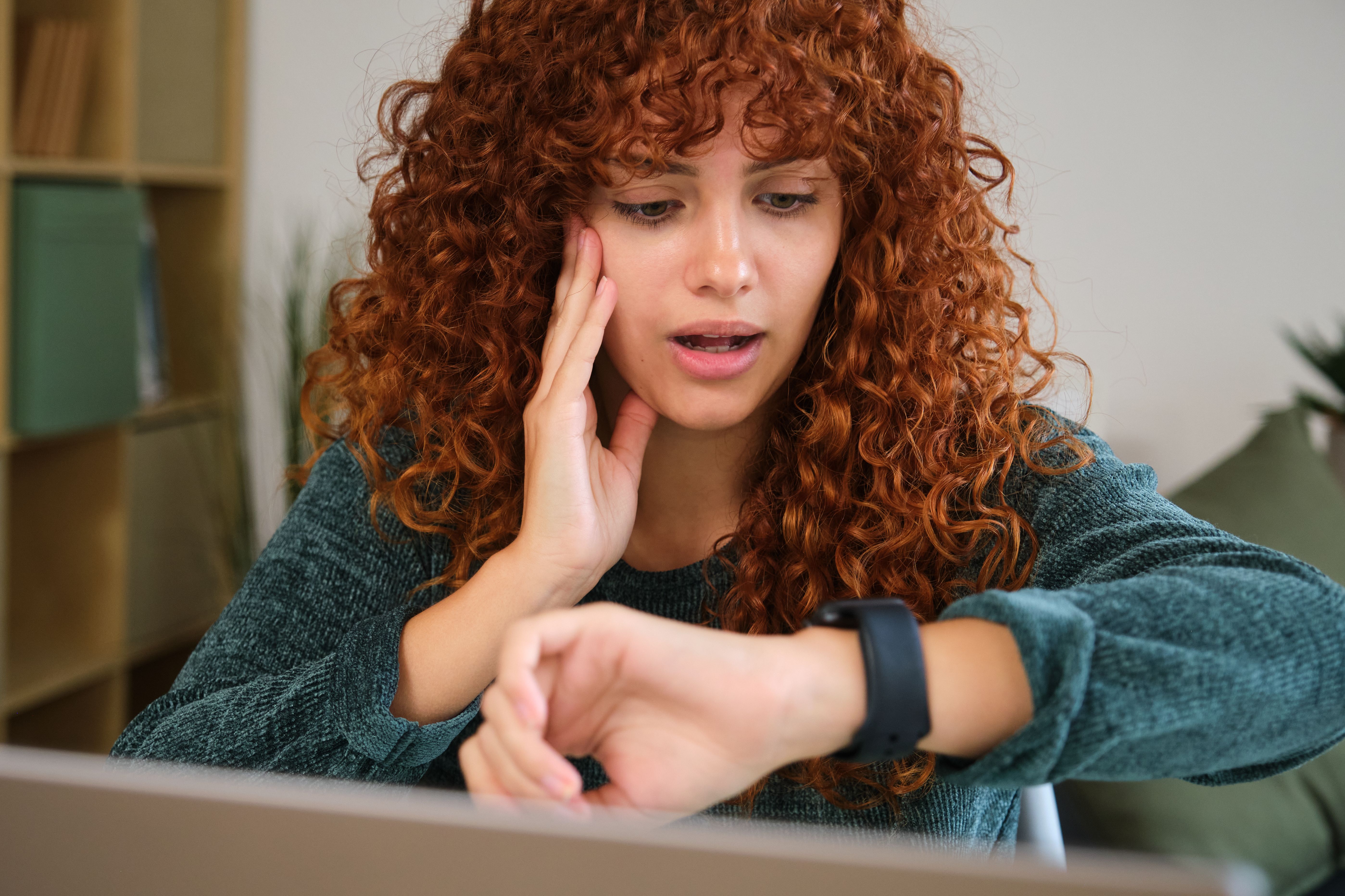 Stressed freelancer woman running late checking smartwatch time working home office