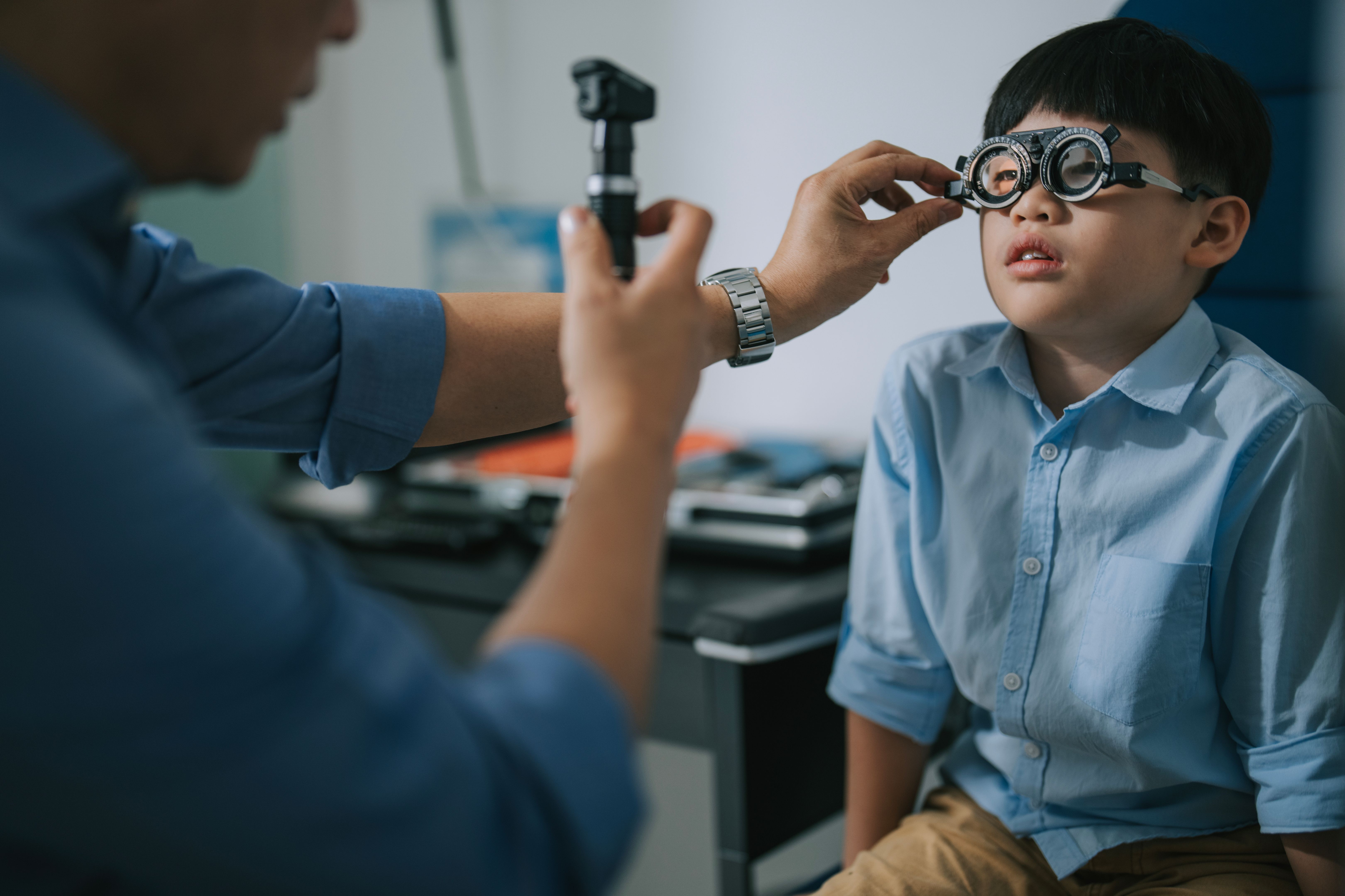 Asian optometrist doing eye test with a boy in clinic