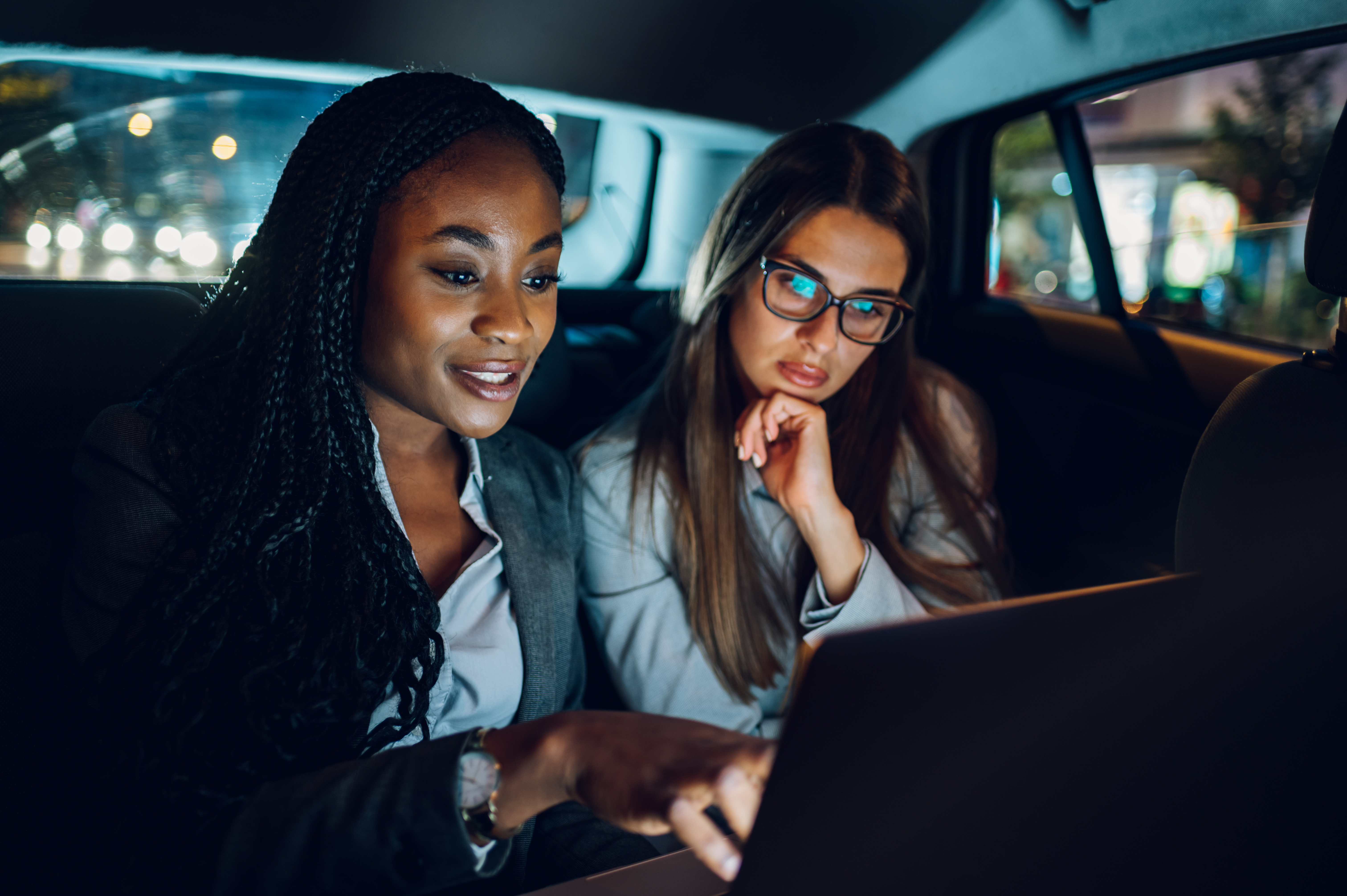 Two multiracial business woman riding in a car and using a laptop Two multiracial business woman riding in a car and using a laptop