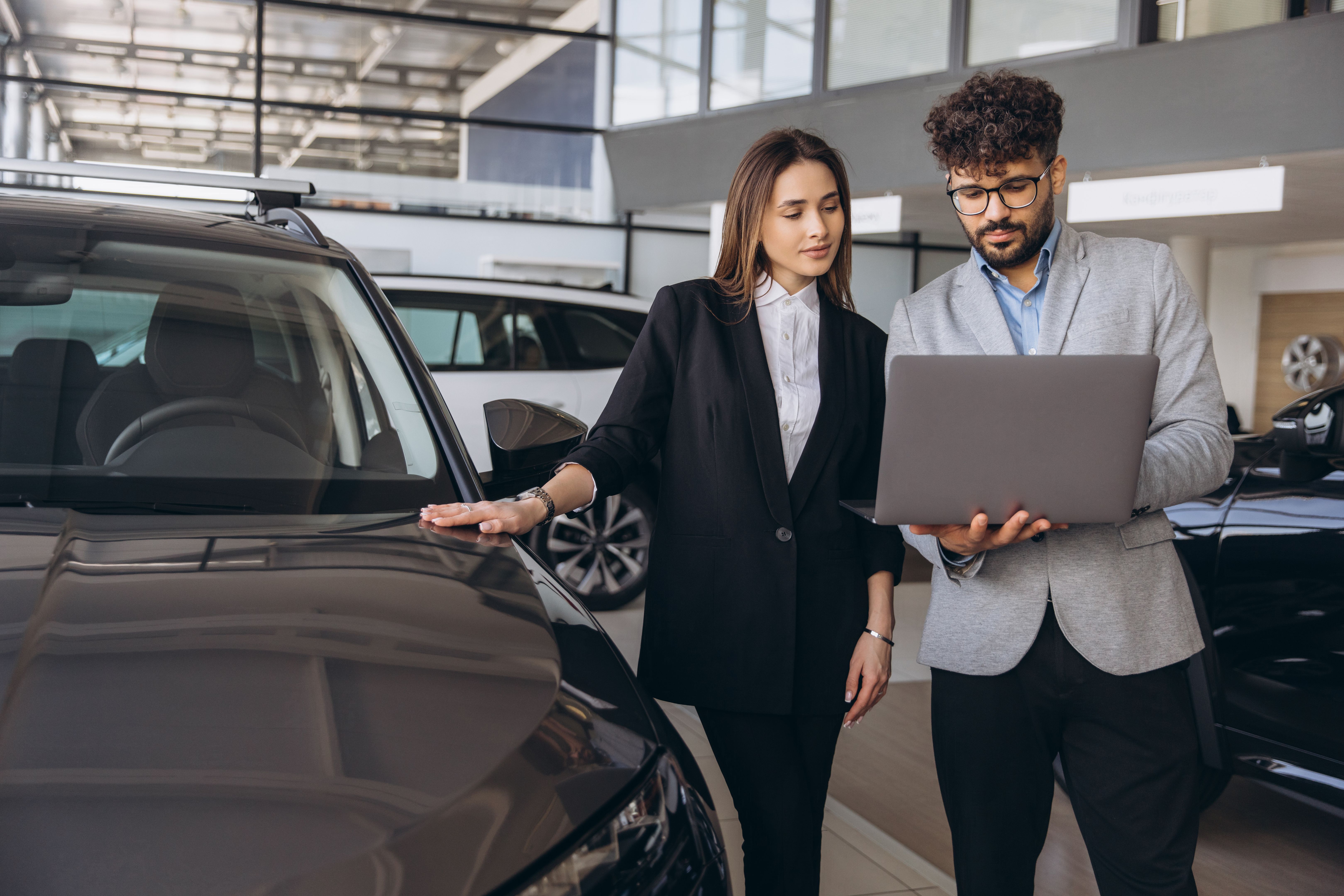 Car salesman showing features on laptop to customer in dealership