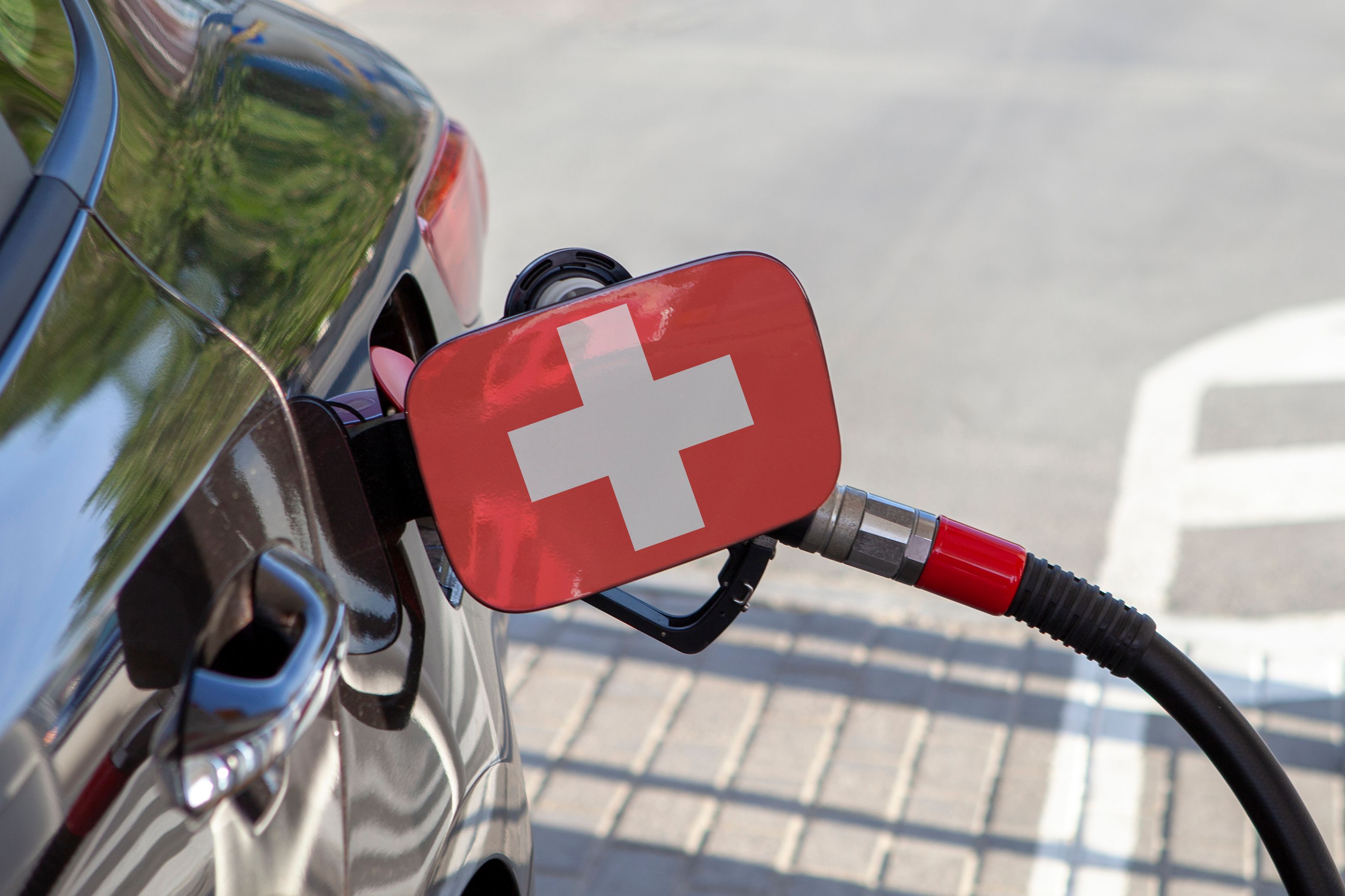 Flag of Suisse on the car's fuel tank filler flap. Fueling car with petrol pump at a gas station. Petrol station. Gasoline and oil products. Close up. Flag of Suisse on the car's fuel tank filler flap. Fueling car with petrol pump at a gas station. Petrol station. Gasoline and oil products. Close up.