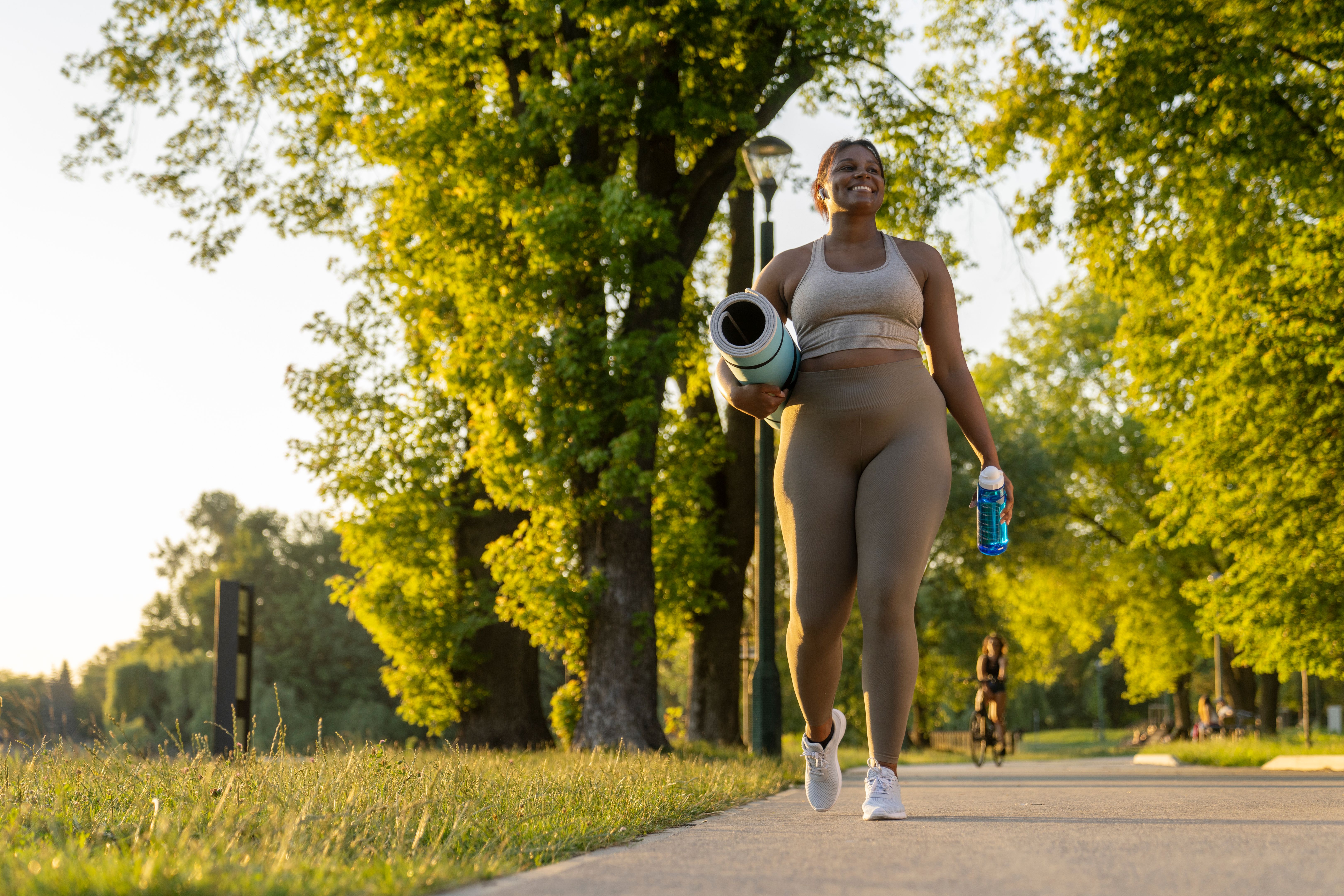 Young African American woman walking with exercise mat and bottle of water through the park in a summer day Young African American woman walking with exercise mat and bottle of water through the park in a summer day