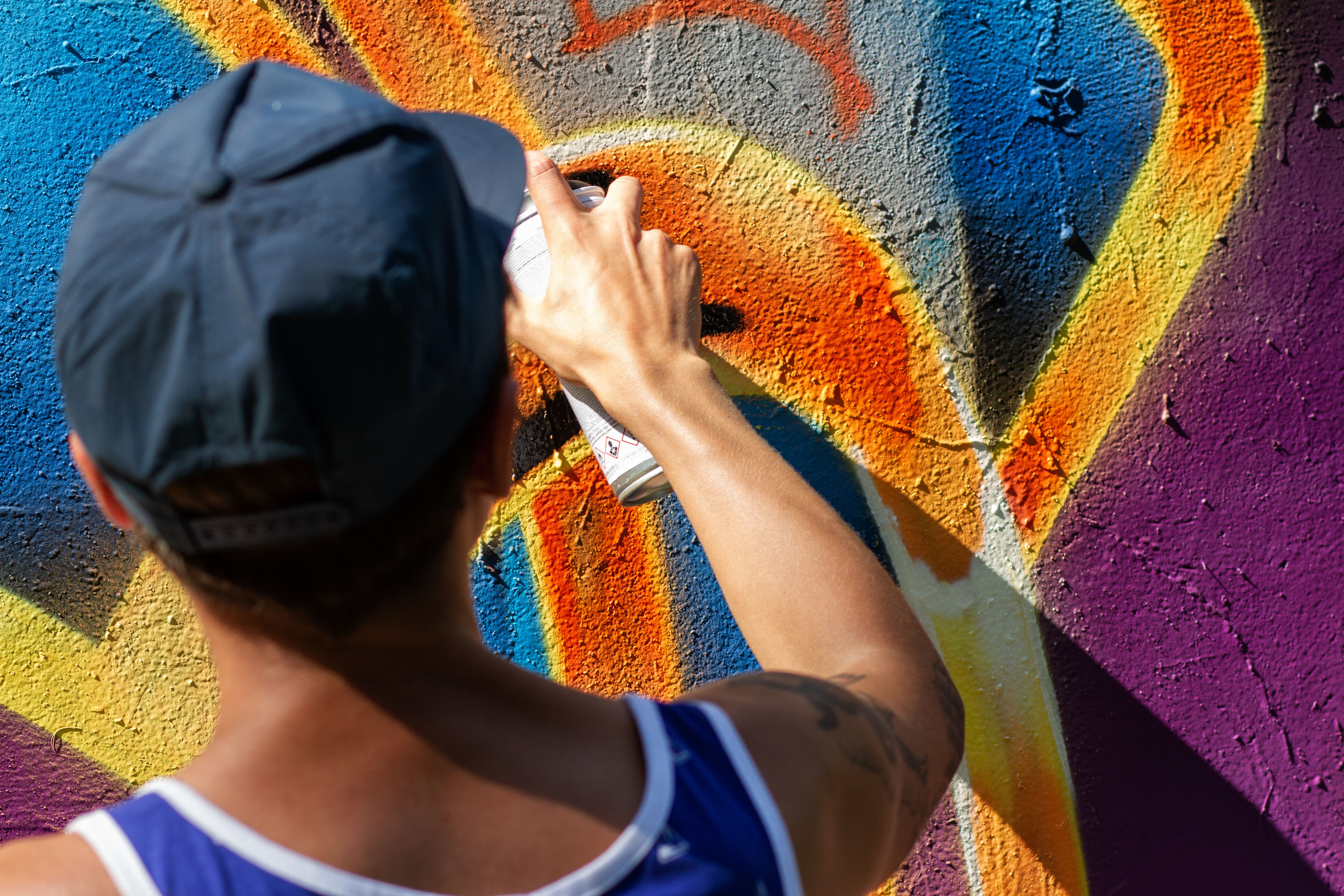 Workshopteilnehmer sprüht mit Cap und Dose ein buntes Graffiti auf eine Wand.