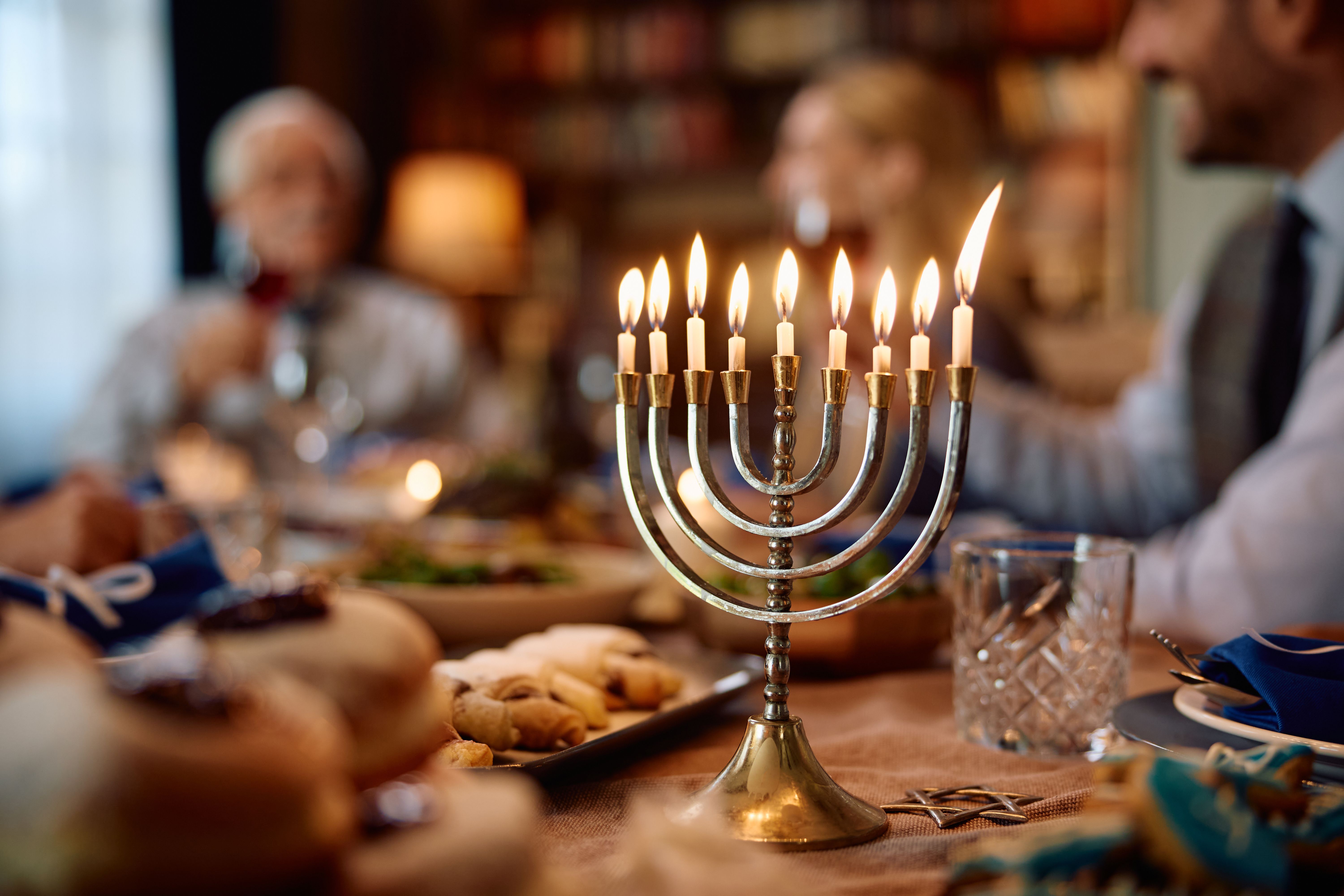 Lit menorah on dining table with Jewish family celebrating Hanukkah in the background.