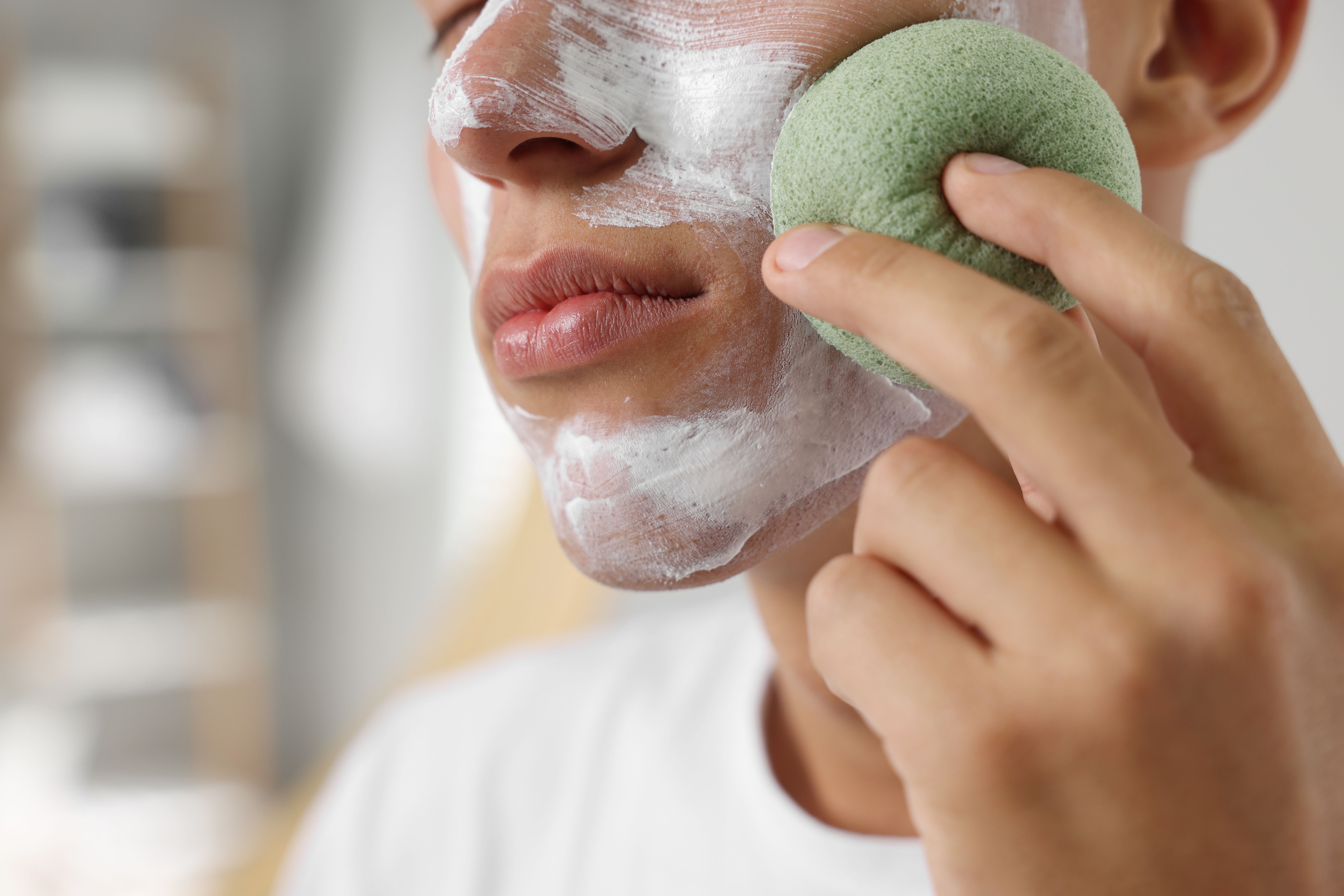 Young man washing off face mask with sponge in bathroom, closeup Young man washing off face mask with sponge in bathroom, closeup