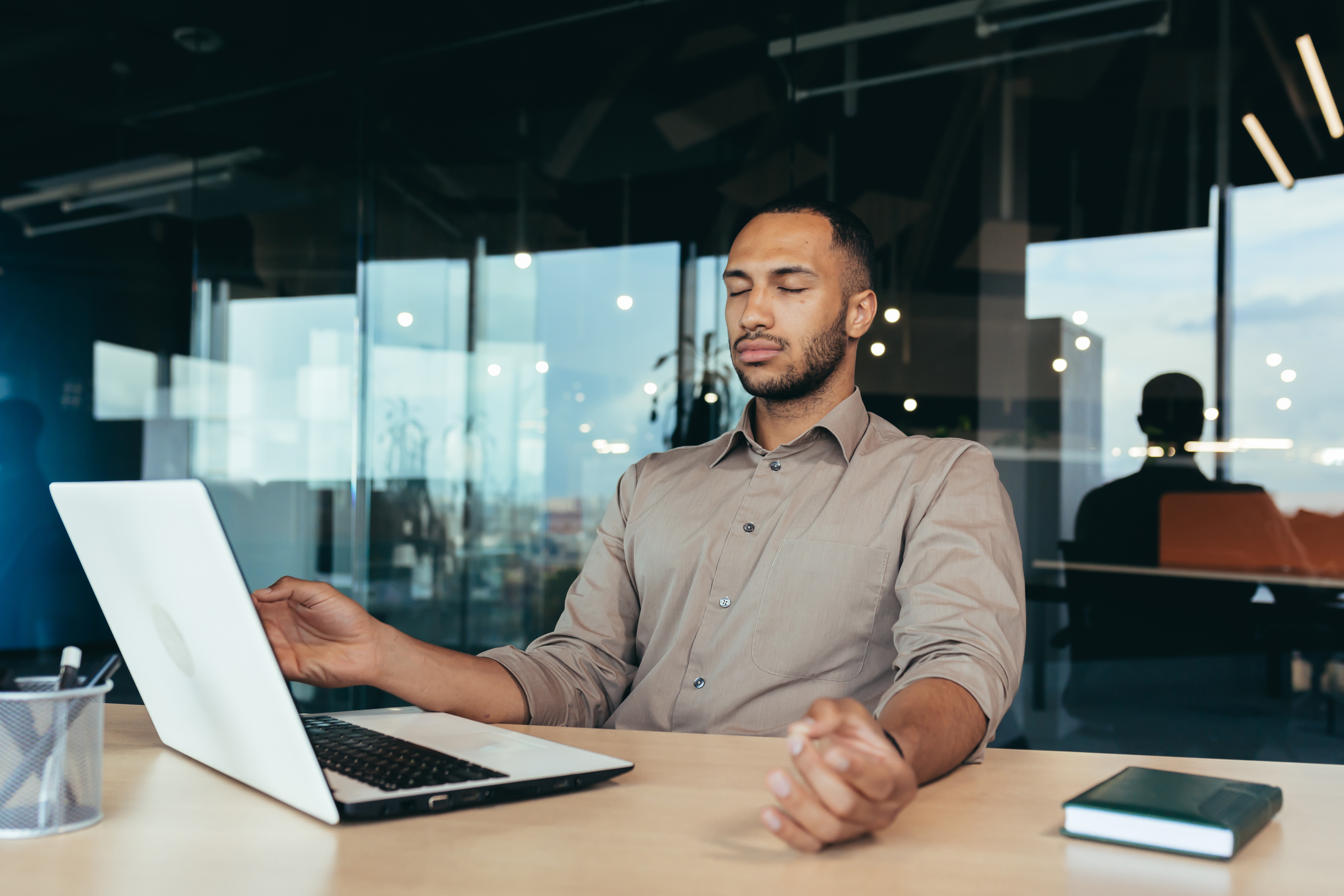 Successful businessman working inside modern office building, man meditating with eyes closed in lotus position sitting on chair Successful businessman working inside modern office building, man meditating with eyes closed in lotus position sitting on chair