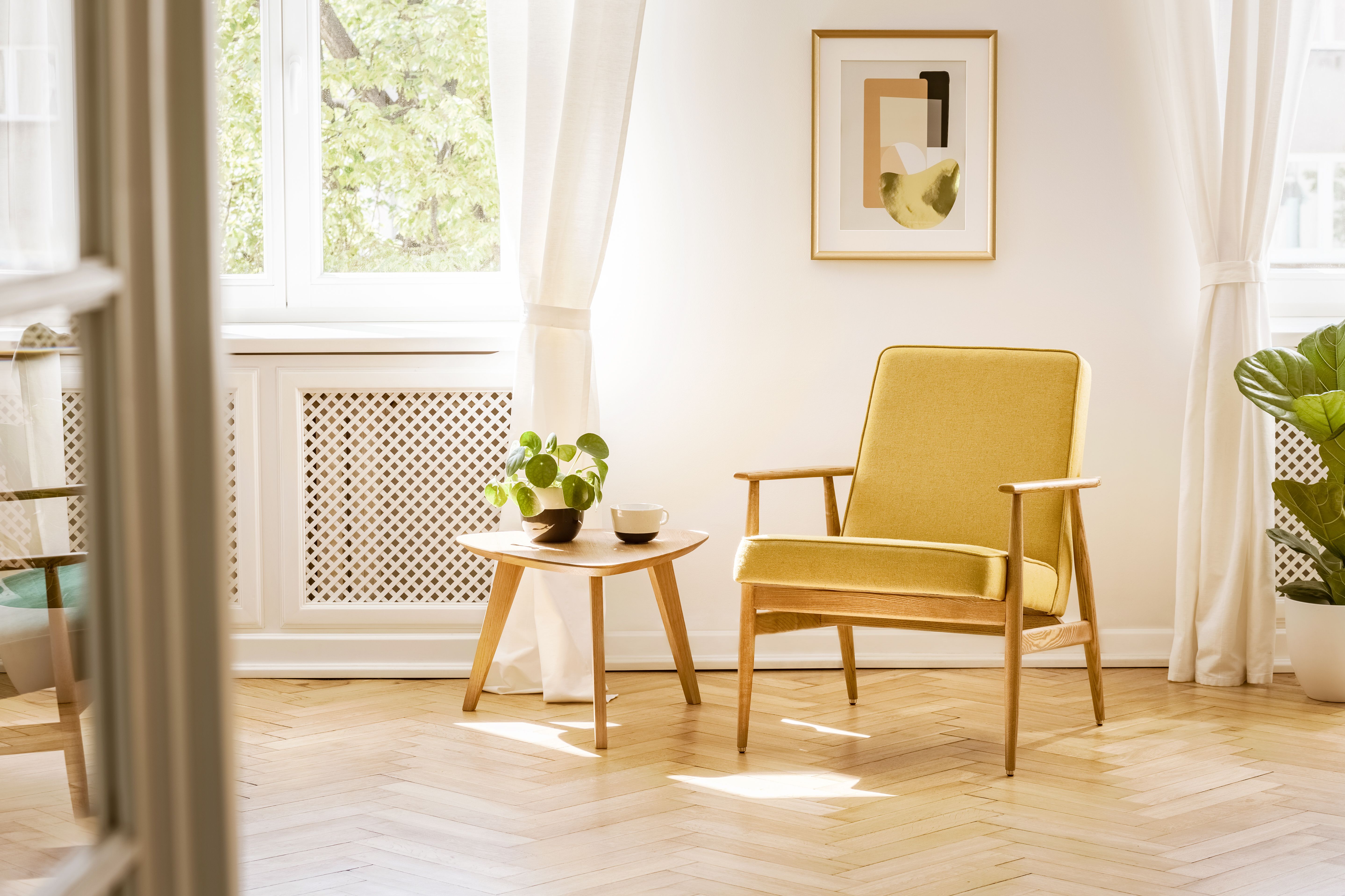 A retro, yellow armchair and a wooden table in a beautiful, sunny living room interior with herringbone floor and white walls. Real photo. A retro, yellow armchair and a wooden table in a beautiful, sunny living room interior with herringbone floor and white walls. Real photo.