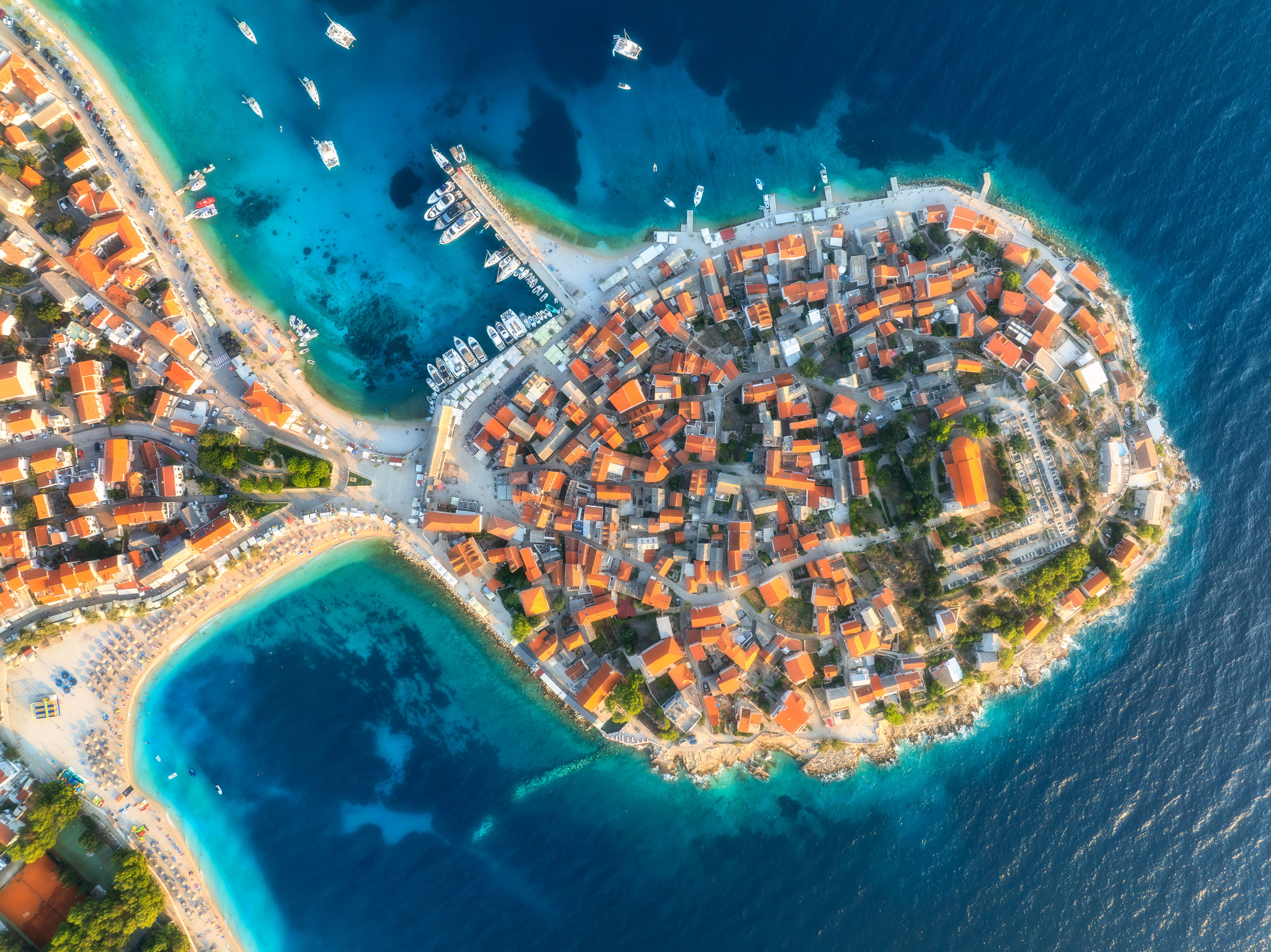 Aeriel view of old town on island at sunset. Summer in Primosten, Croatia, Adriatic Sea. Top drone view of houses, clear blue water, marina with boat and yachts, sandy beach. Travel. Aerial landscape
