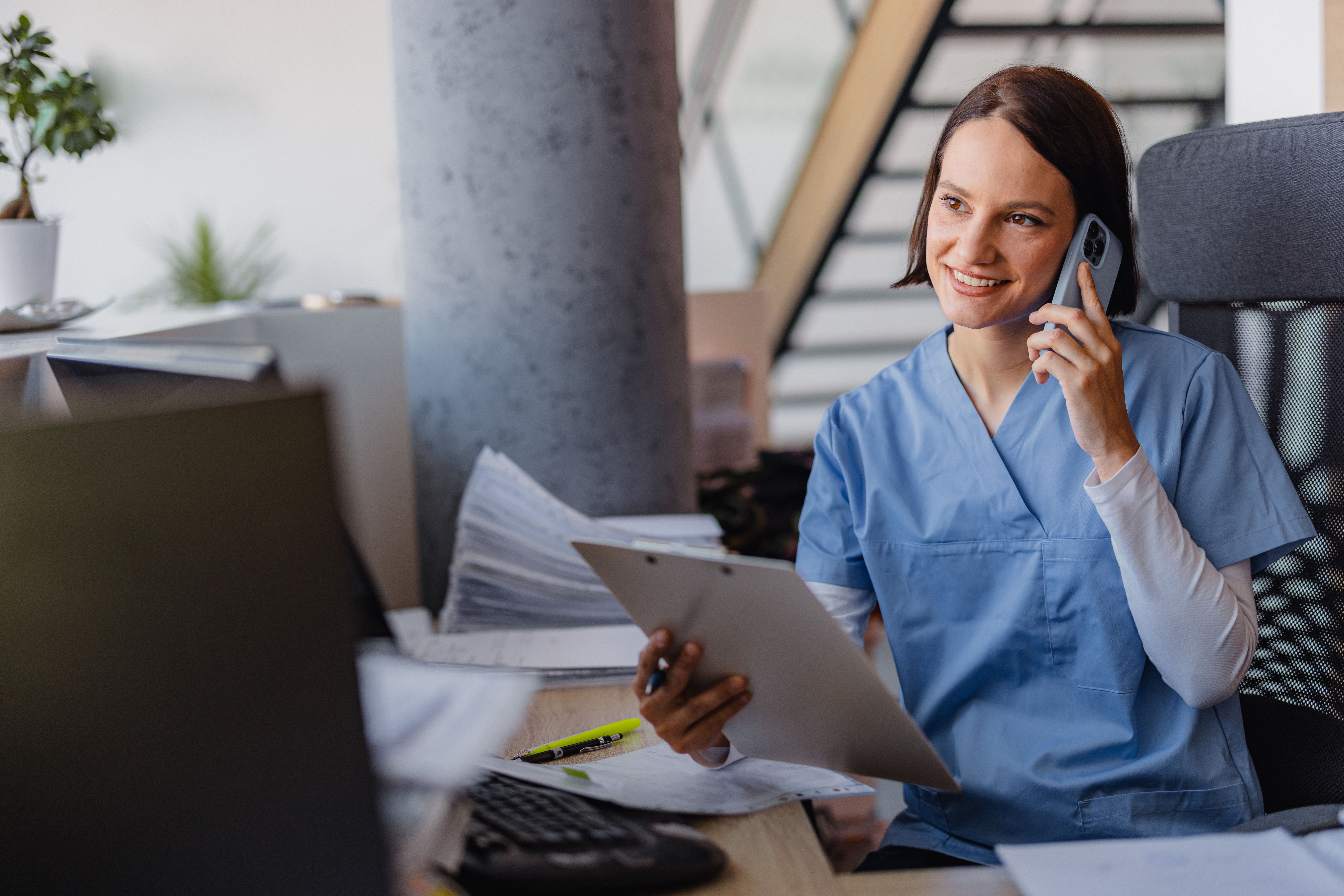 Young female receptionist talking on phone in clinic while sitting and looking on pc monitor