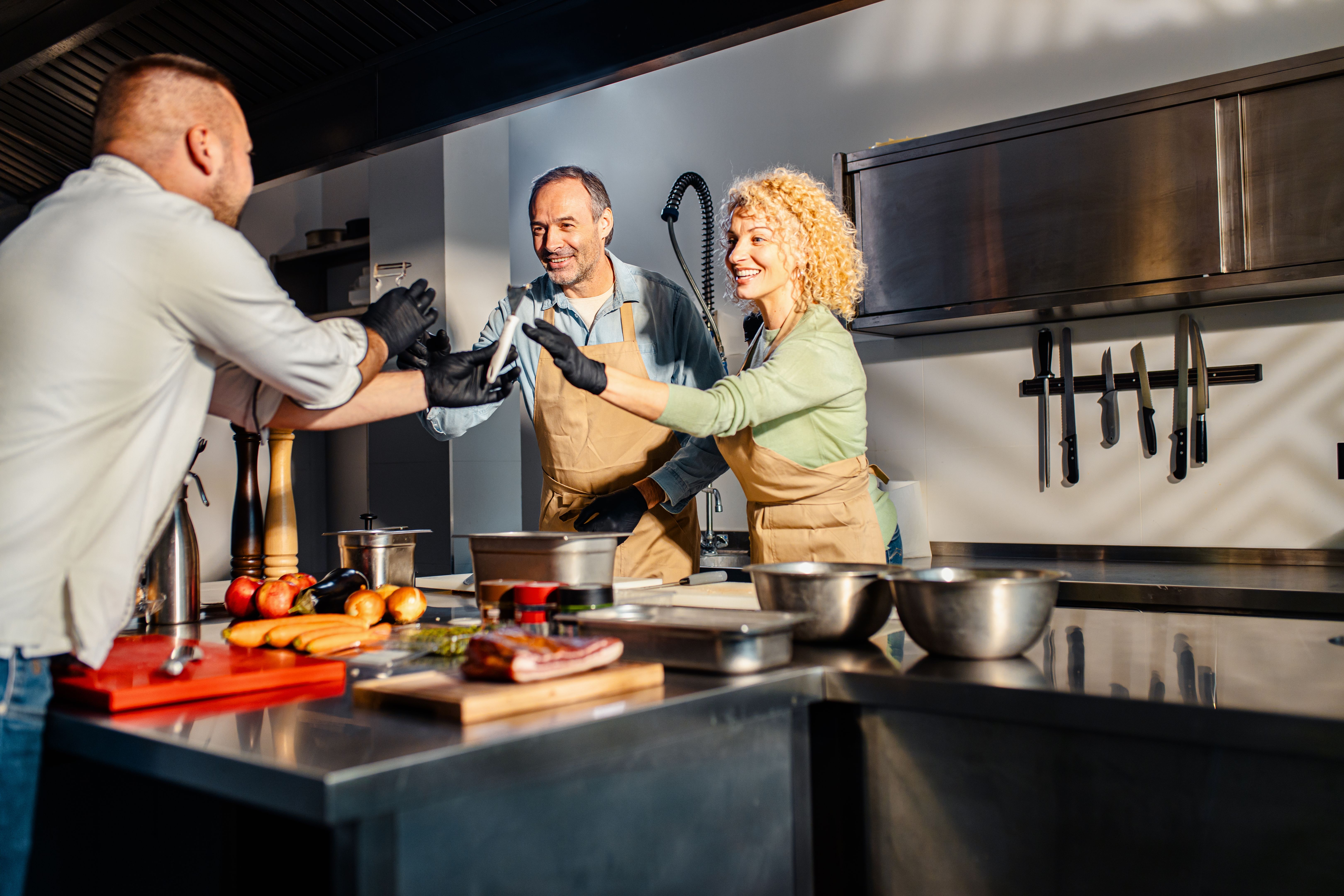 Middle-aged couple enjoying a cooking class with a chef preparing carrot for a meal in the kitchen. Middle-aged couple enjoying a cooking class with a chef preparing carrot for a meal in the kitchen.