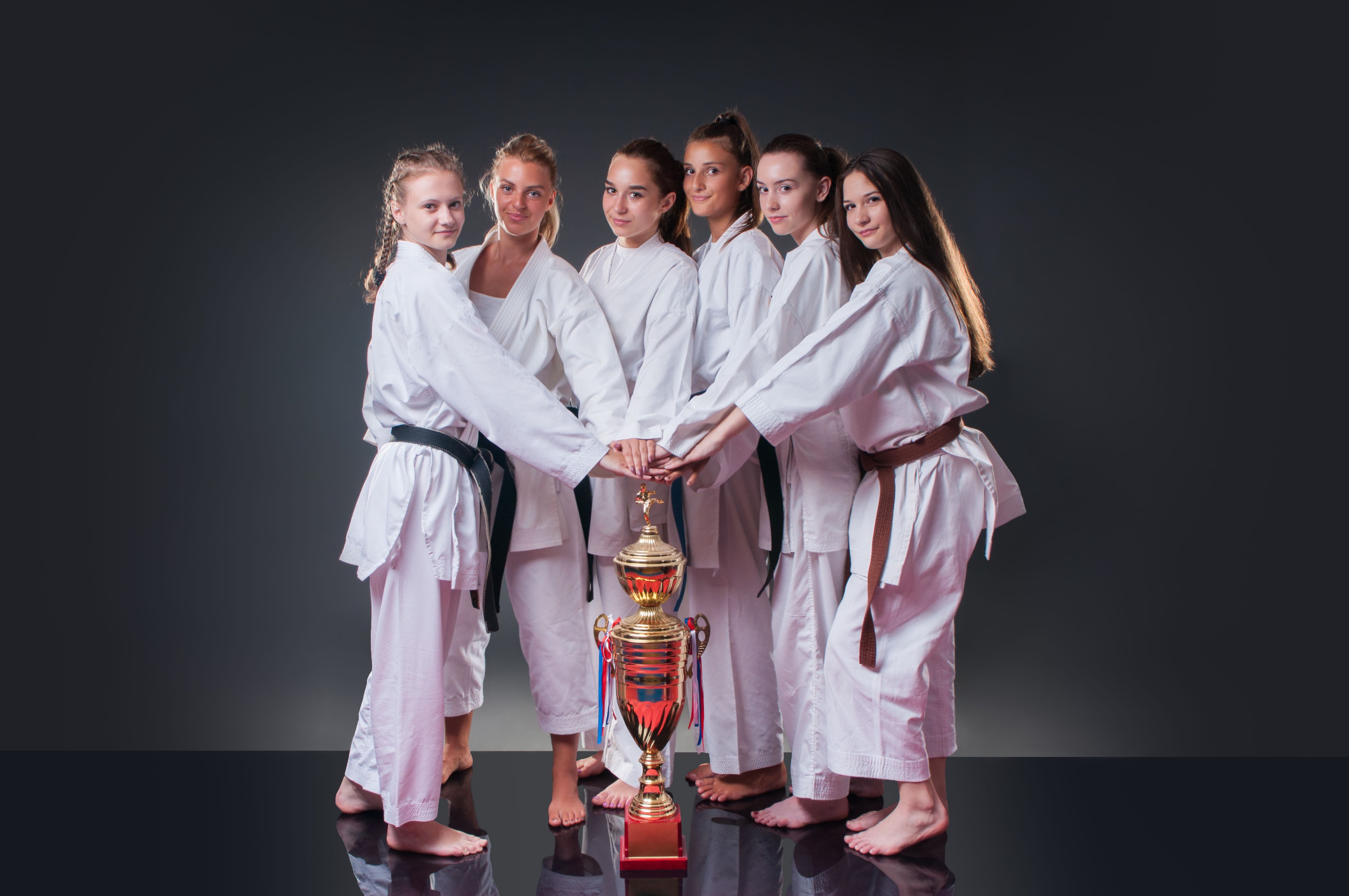 Group of beautiful female karate players posing with the cup on the gray background. Celebrating 1st place.