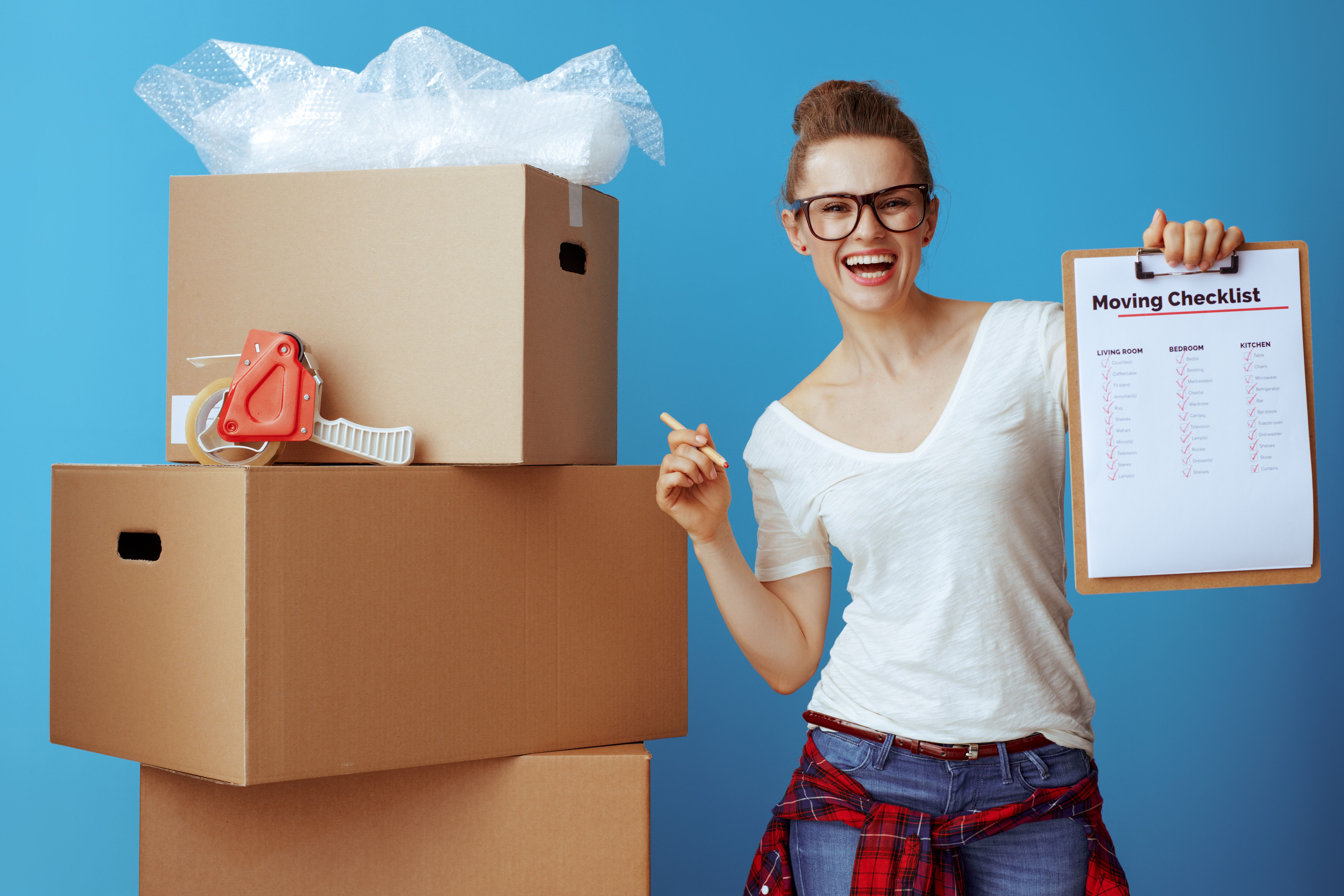 happy woman near cardboard box showing moving checklist on blue happy woman near cardboard box showing moving checklist on blue