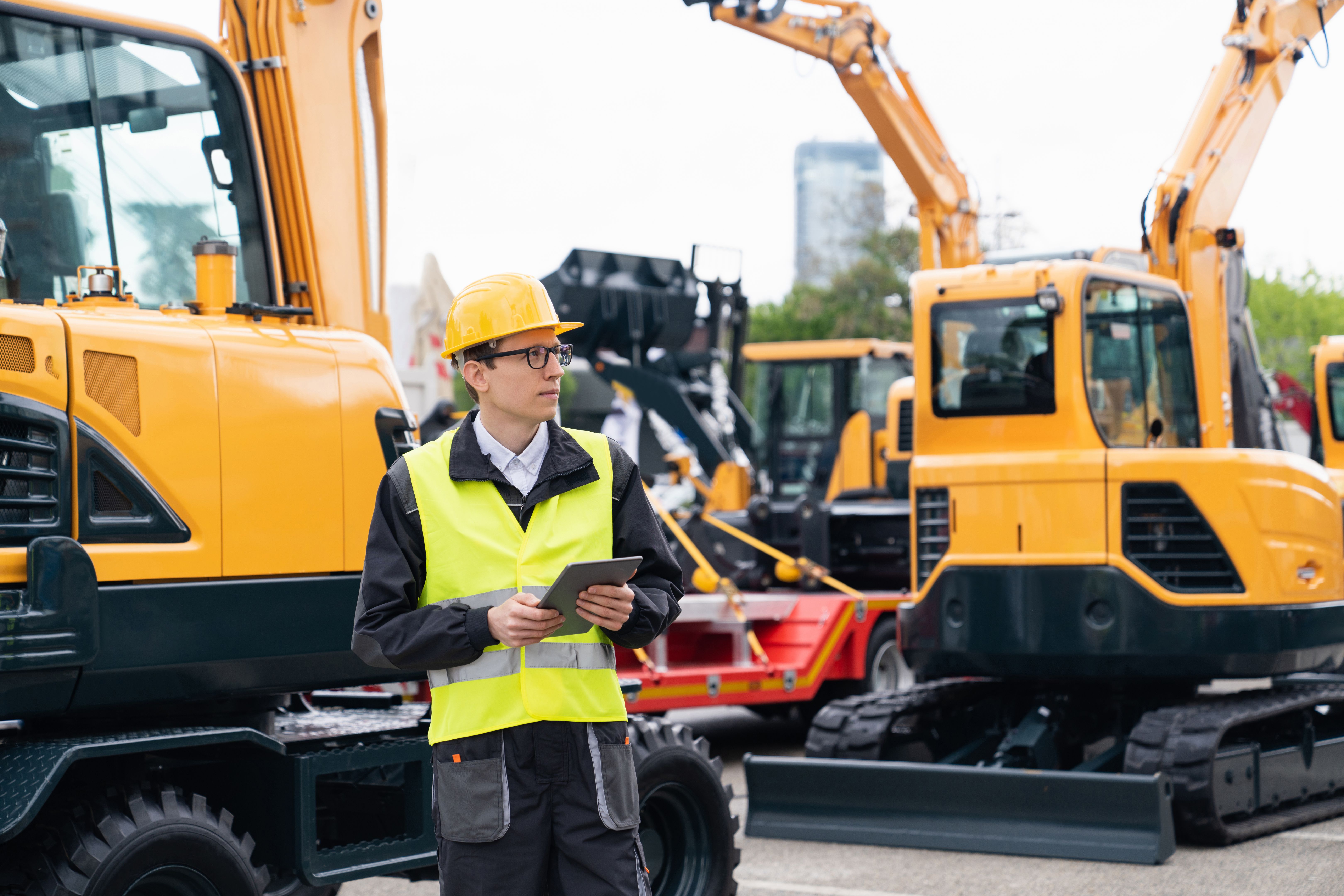 Ingegnere in un casco con una tavoletta digitale accanto agli escavatori