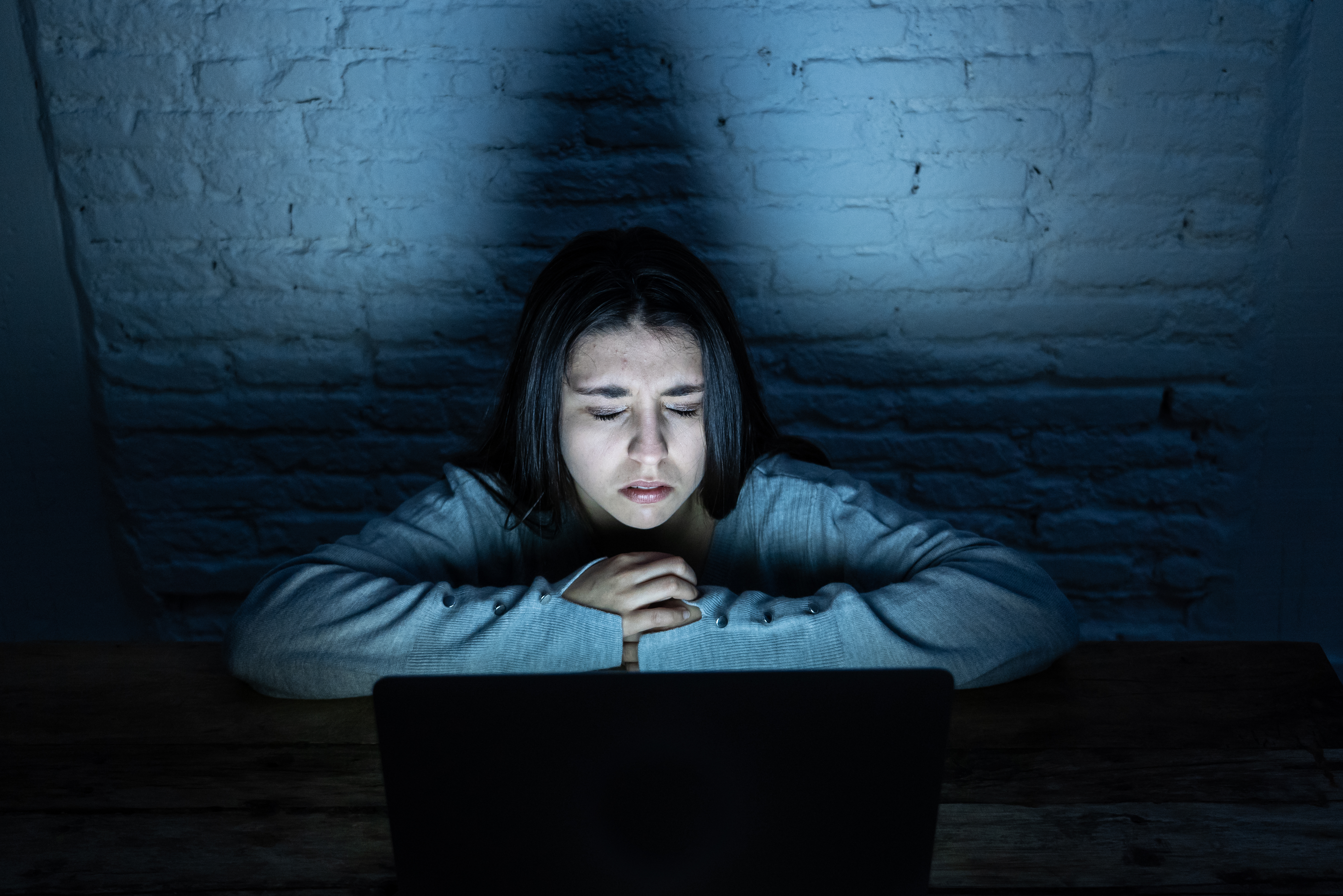 Dramatic portrait of sad, scared young woman on laptop suffering cyber bullying and harassment.