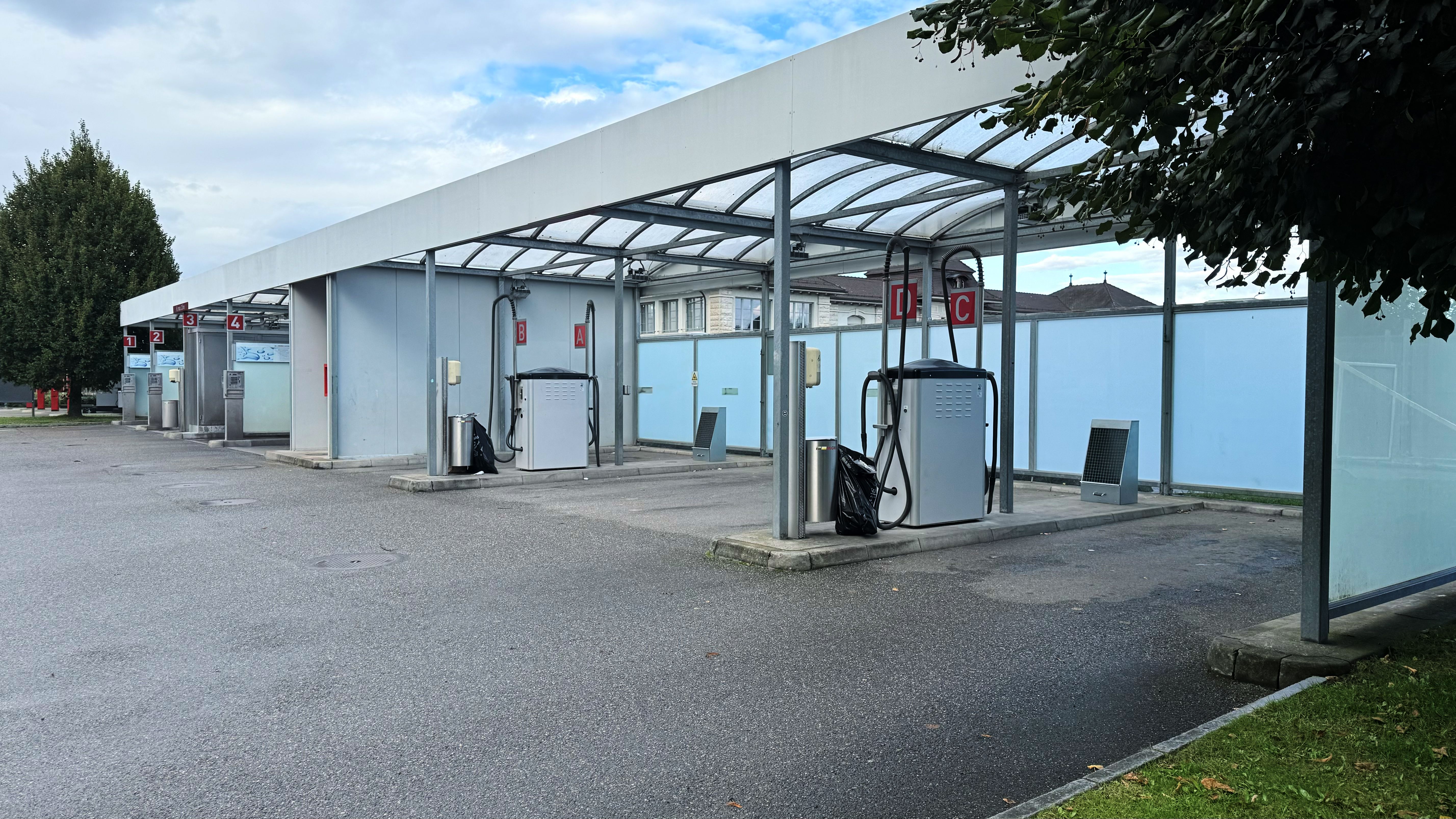 Outdoor self-service car wash bays with metal canopy and pressure washer hoses, empty washing station on asphalt, diagonal front view