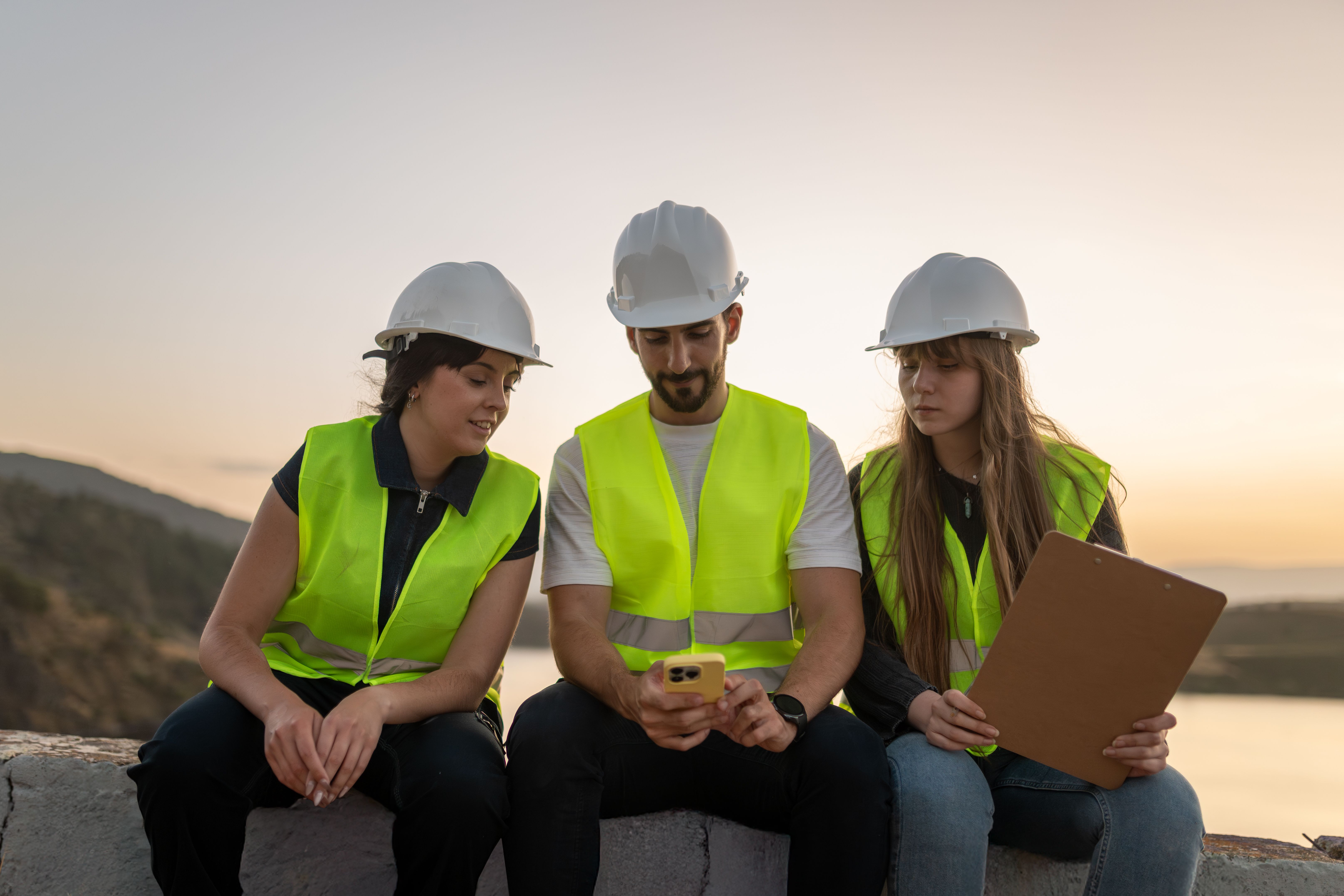 Ingenieros usando una aplicación móvil en el sitio de construcción durante la puesta del sol