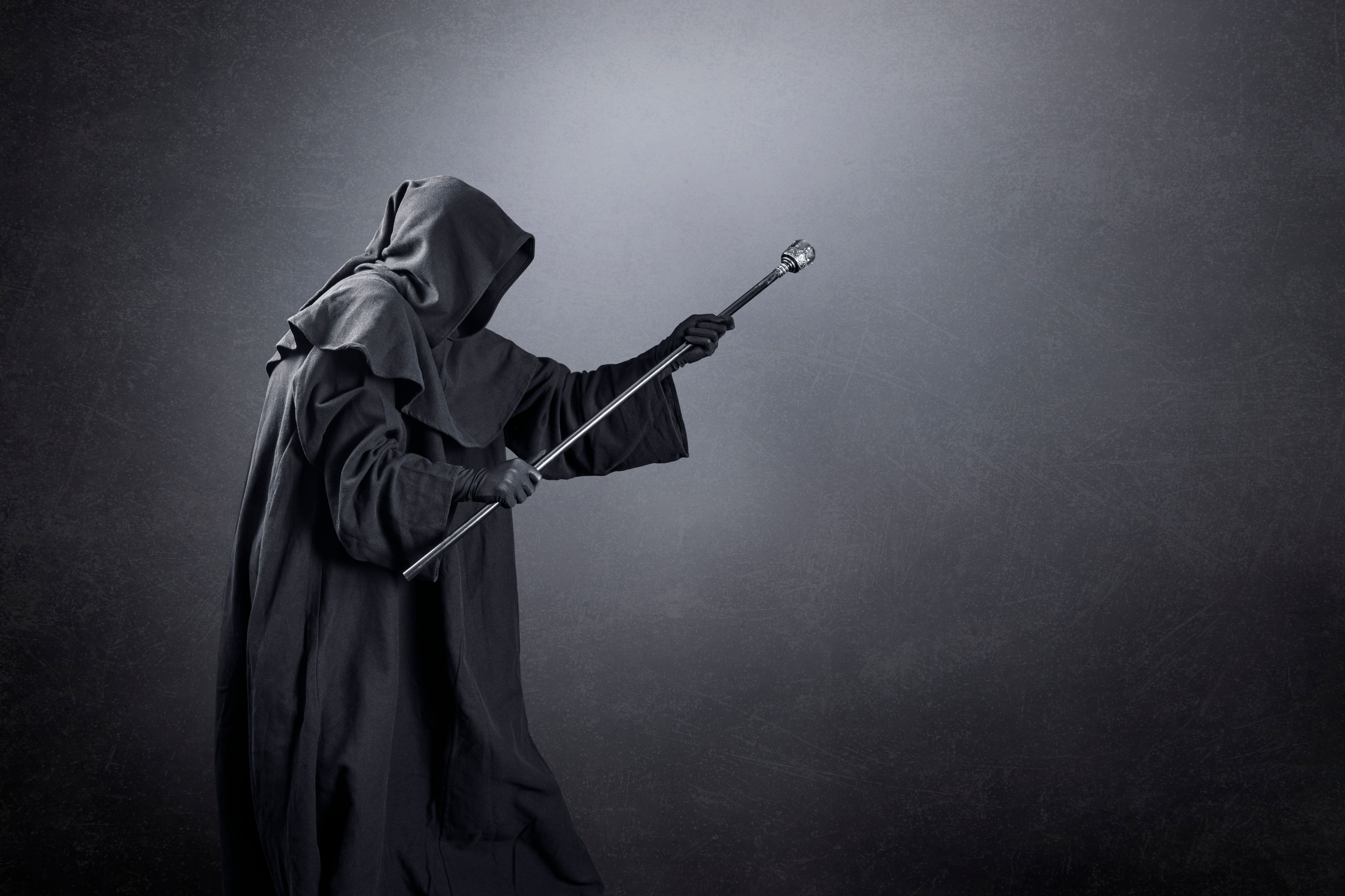 Wizard with hooded cape and magic staff over dark misty background Wizard with hooded cape and magic staff over dark misty background