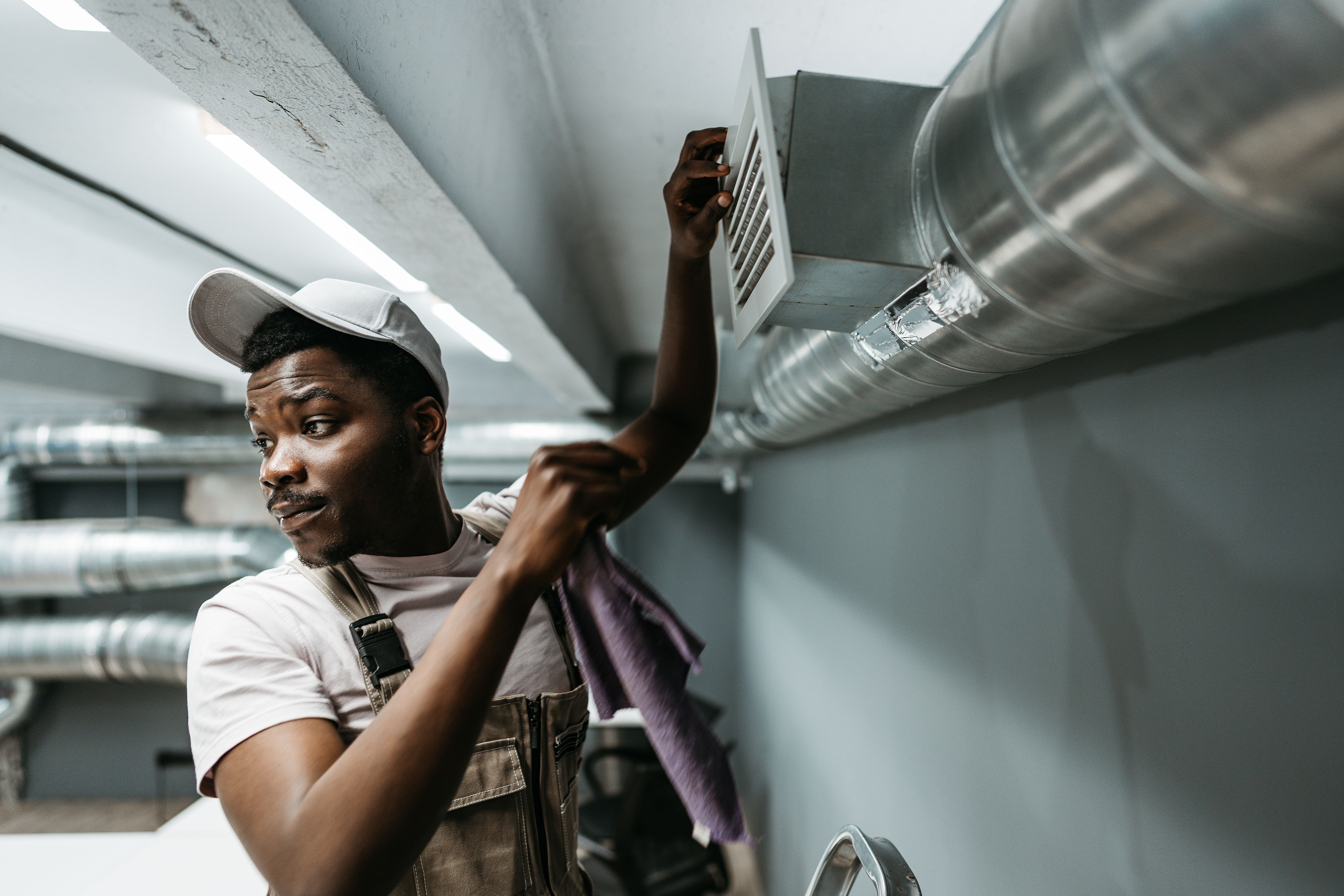 Worker performs maintenance on ventilation system in commercial building during daytime hours