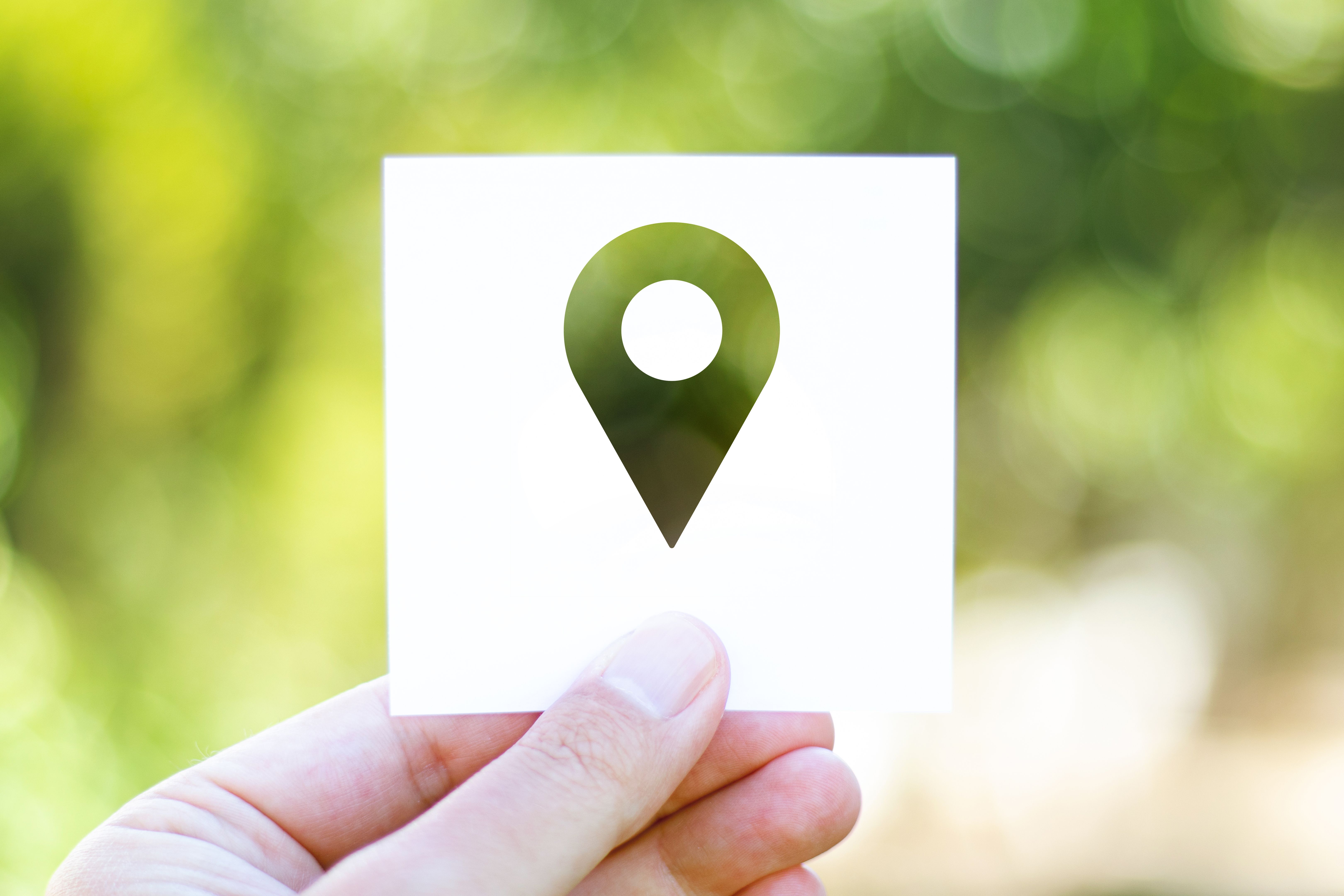 Holding the paper with Pin Icon in front of a beautiful blur nature background