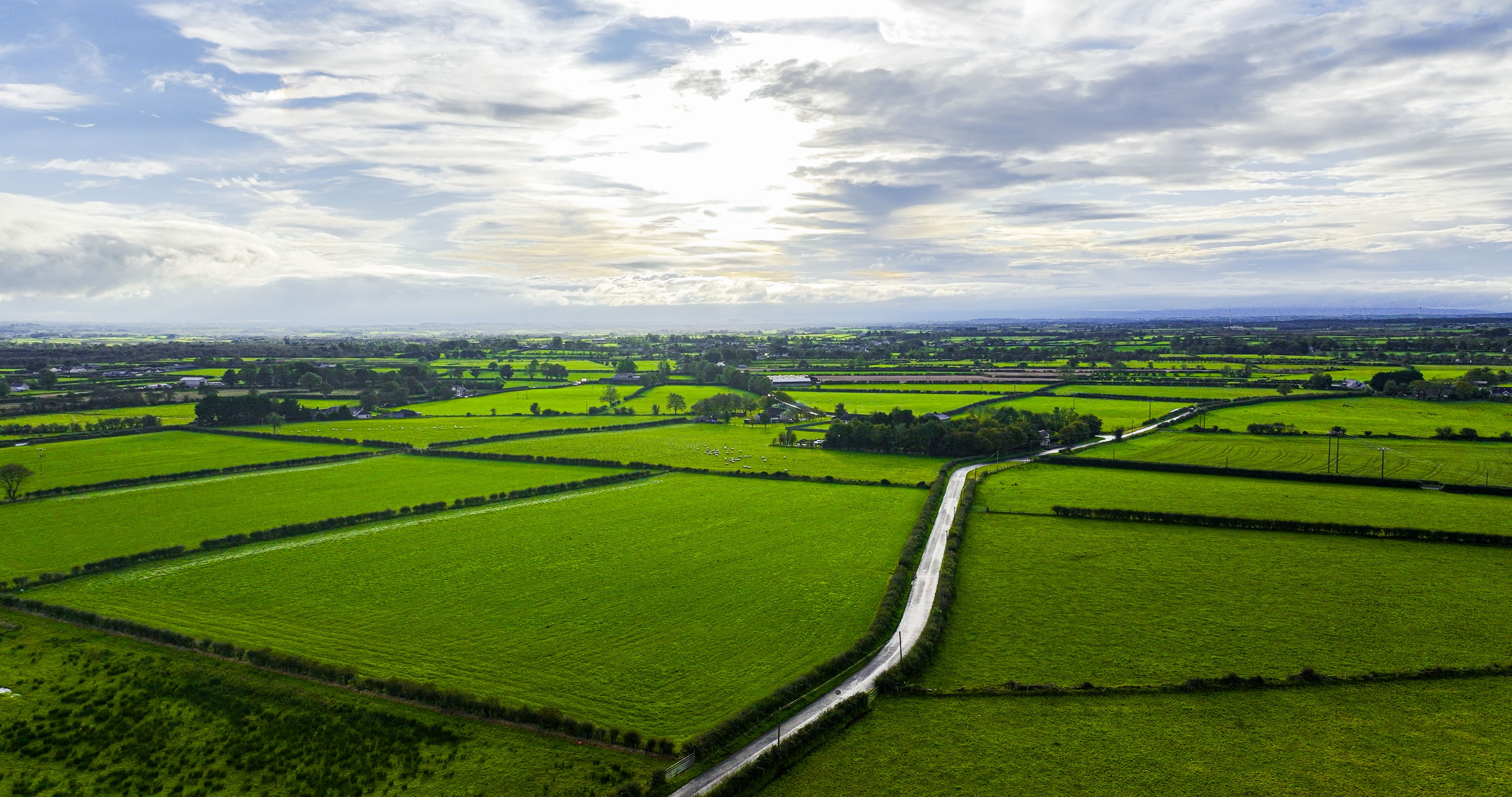 Aerial view of flat green land in Northern Ireland at sunset, Aerial view of green cultivated farmland with growing crops and distant village houses on bright summer evening, Aerial view of Northern Ireland sky cloudscape