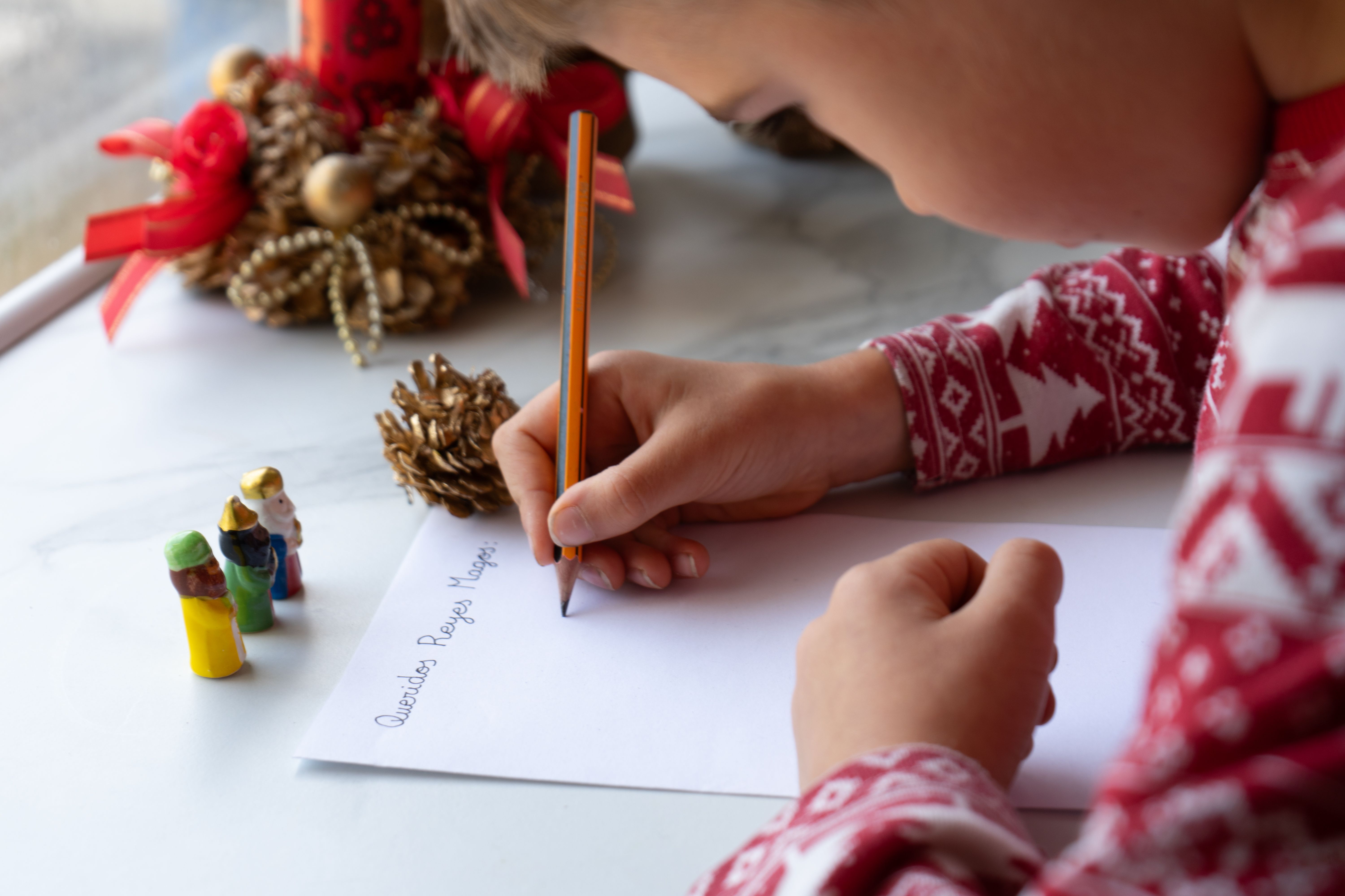 Niño escribiendo carta a los Reyes Magos cerca de la decoración navideña