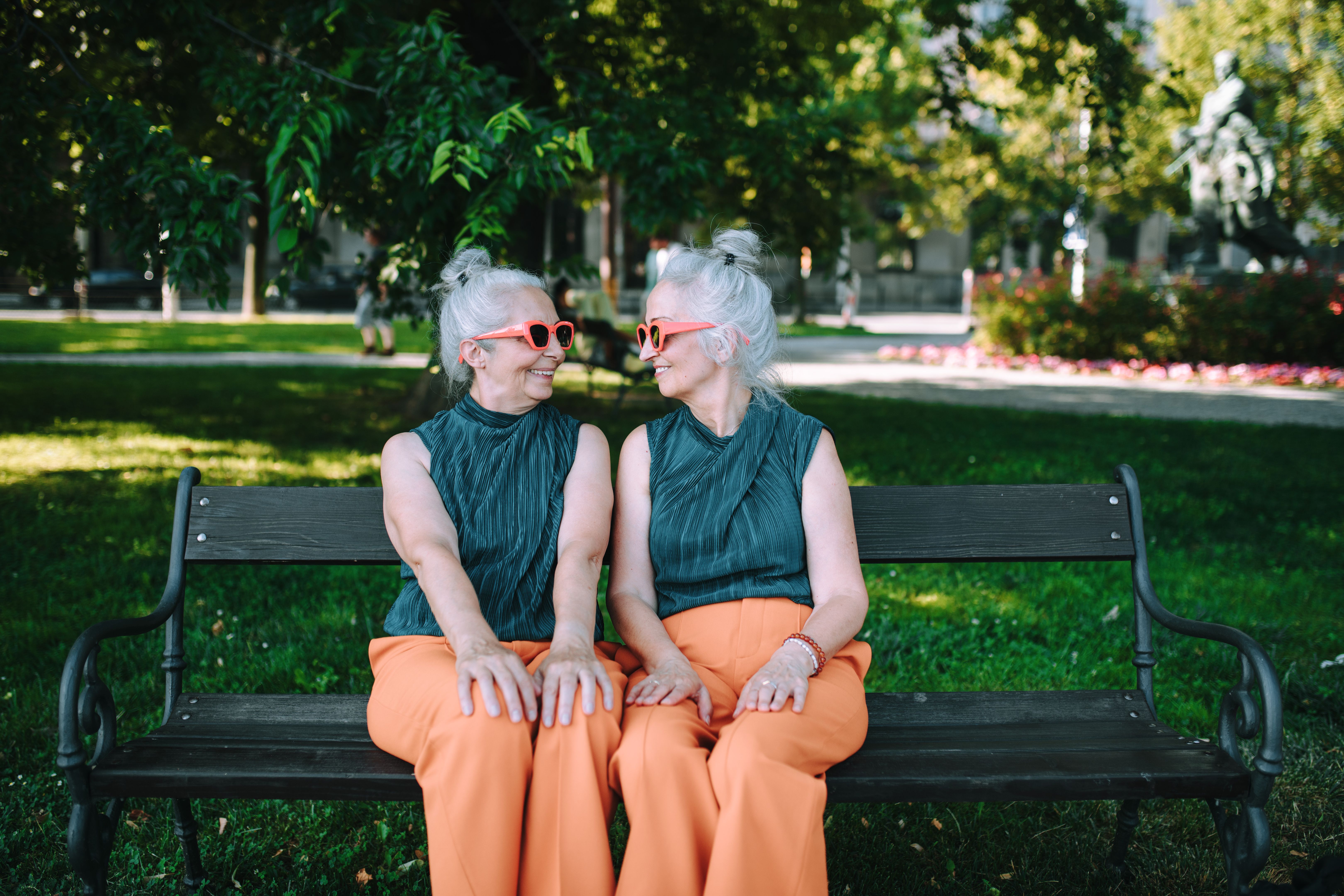 Happy senior sister, twins sitting in city park and resting after shopping.