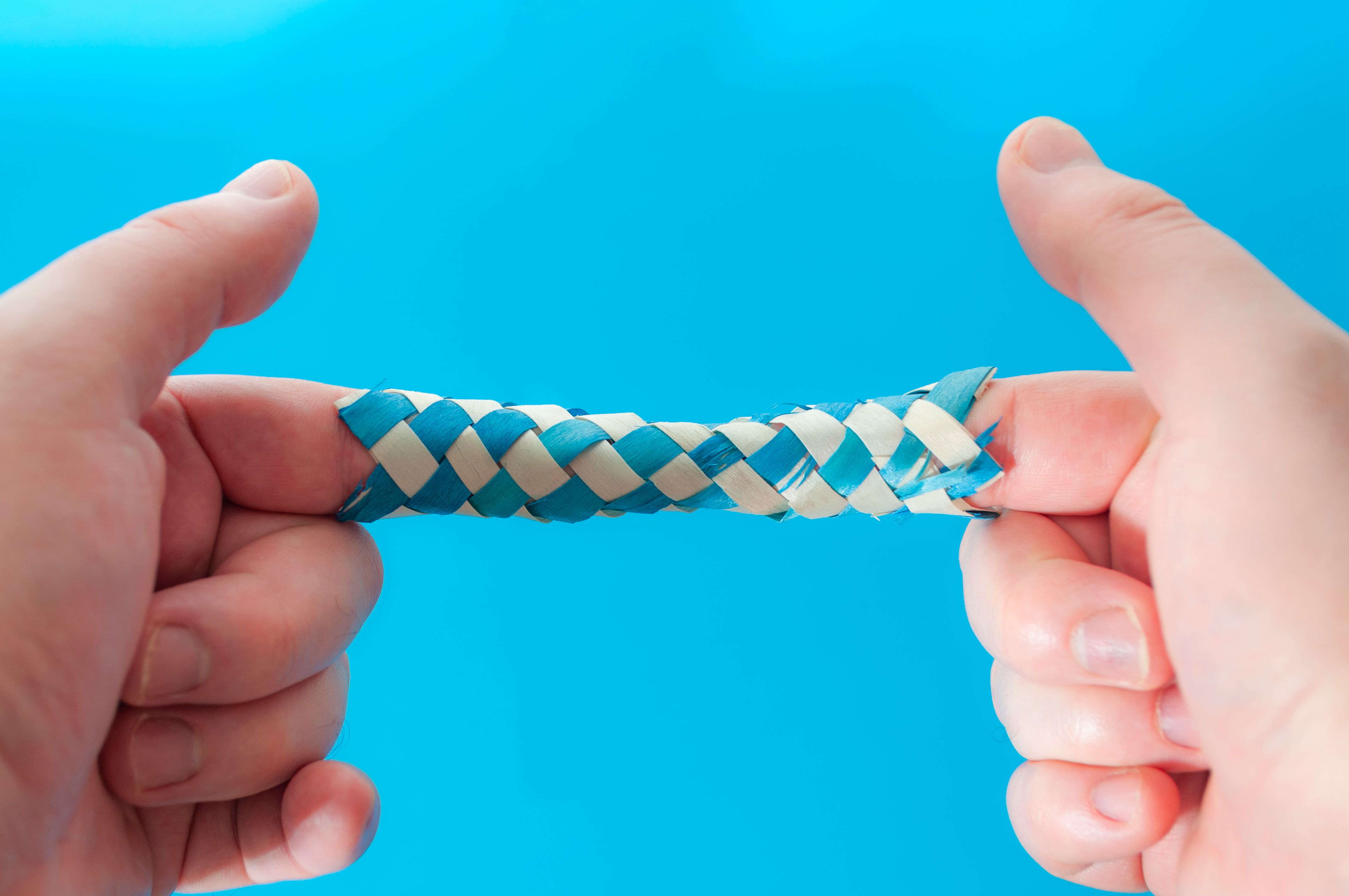 Puzzle game and logic games concept with hands playing with a chinese finger trap, a toy that the more you pull the tighter it gets stuck and you need to push to escape isolated on blue background