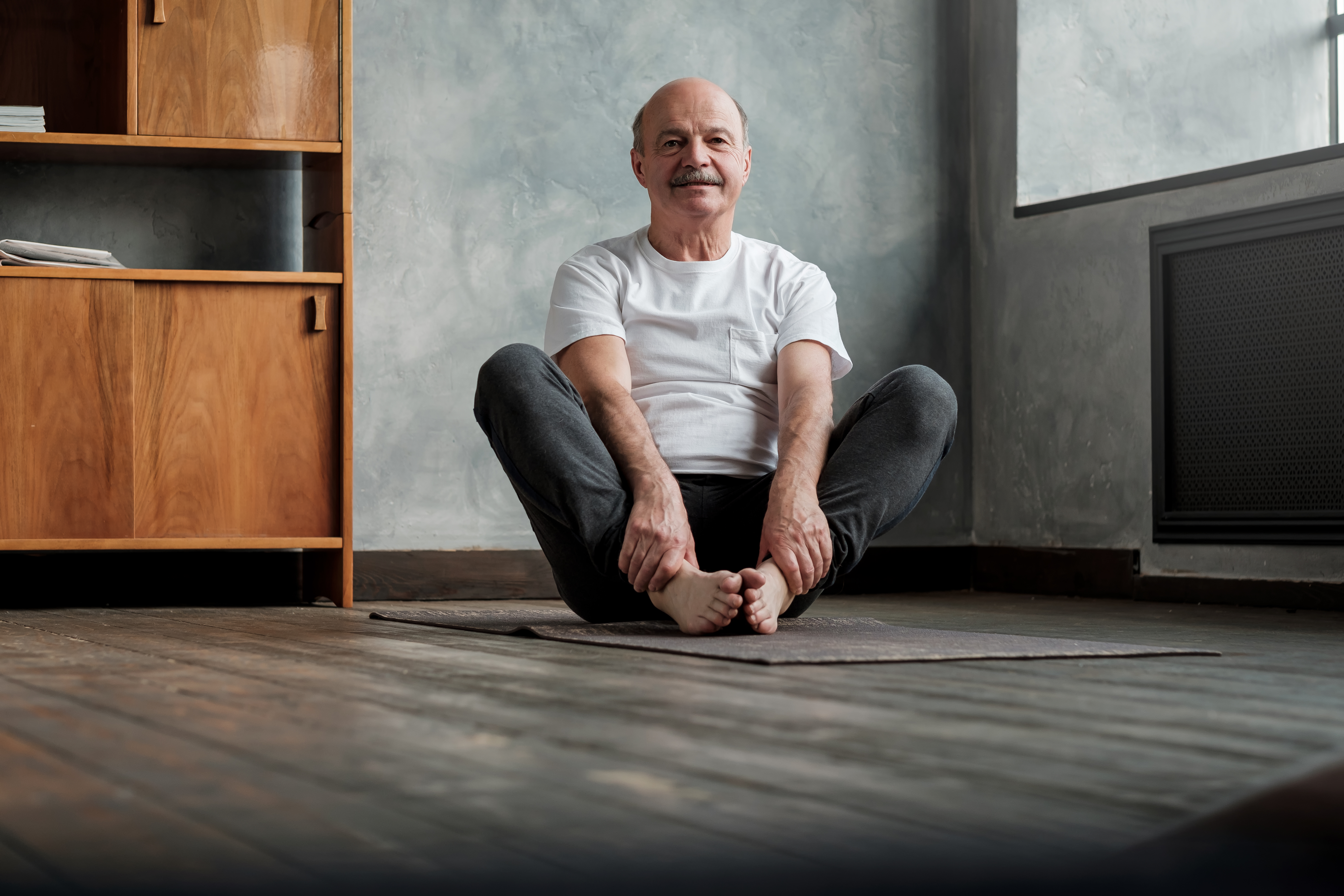 Mature hispanic man sitting barefooted on mat, doing baddha konasana pose Mature hispanic man sitting barefooted on mat, doing baddha konasana pose