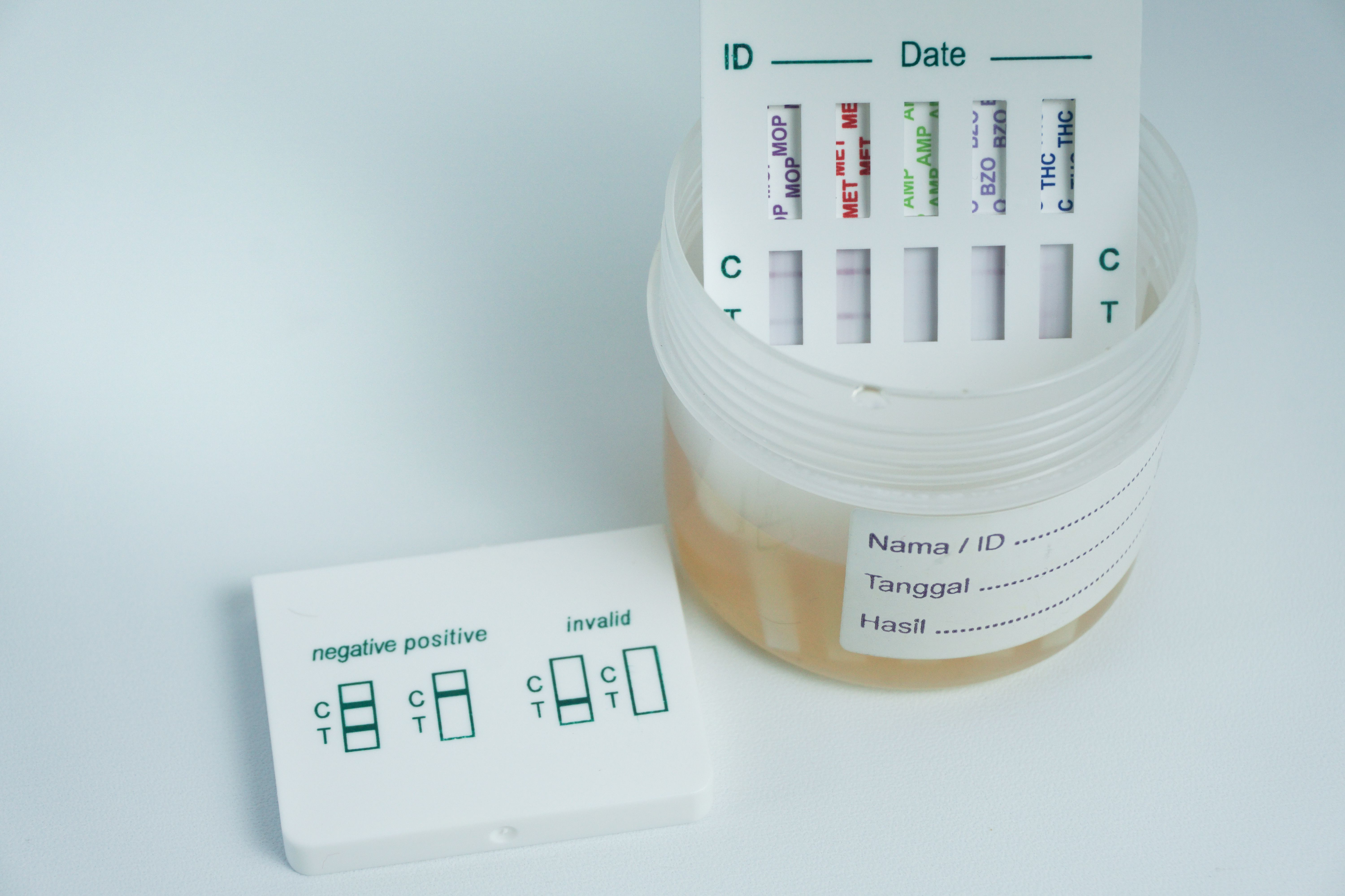 Examination of narcotic content in urine by placing the urine in a urine container and then immersing a portion of the drug test kit in the urine. isolated on white Examination of narcotic content in urine by placing the urine in a urine container and then immersing a portion of the drug test kit in the urine. isolated on white