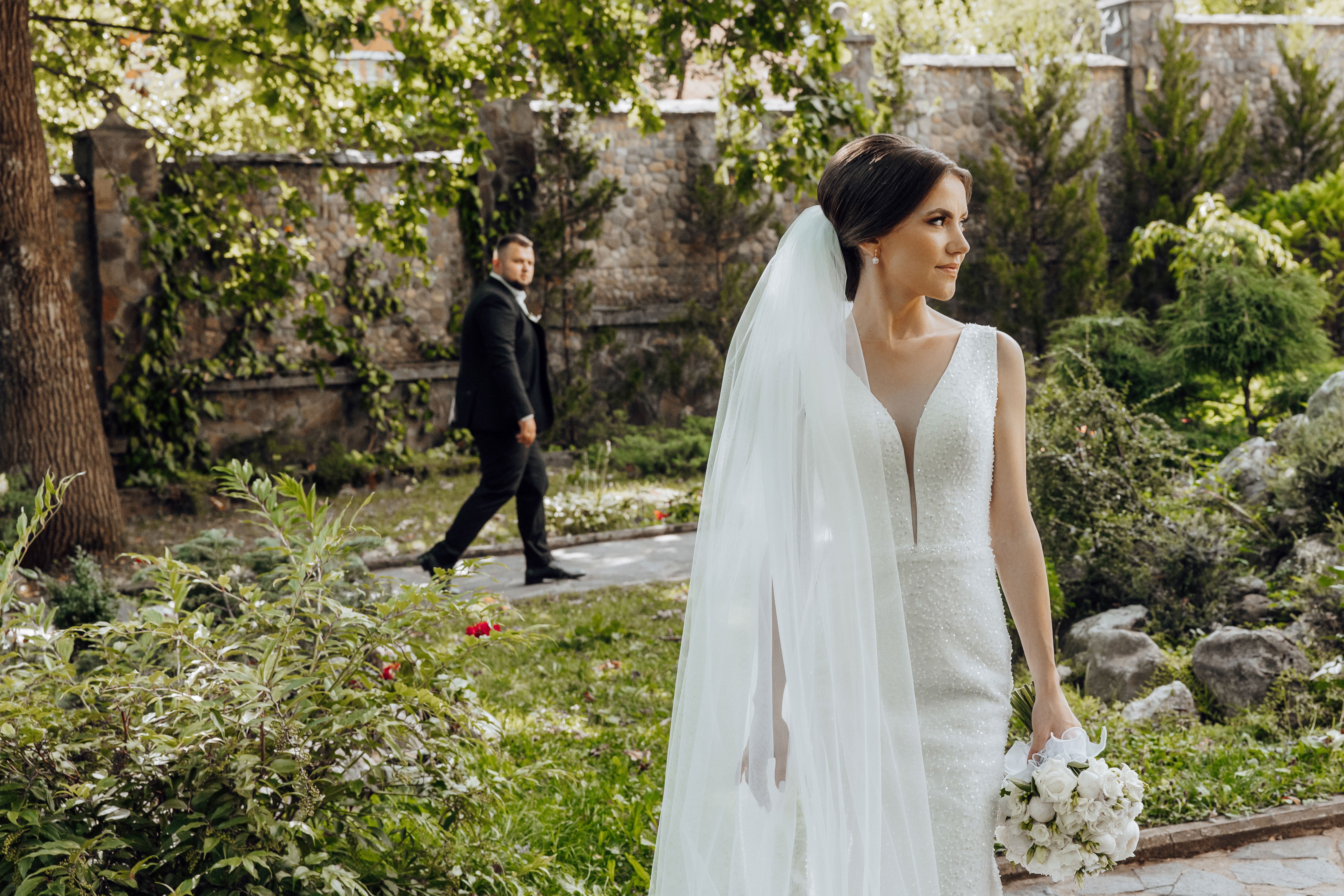 A bride and groom are walking through a garden