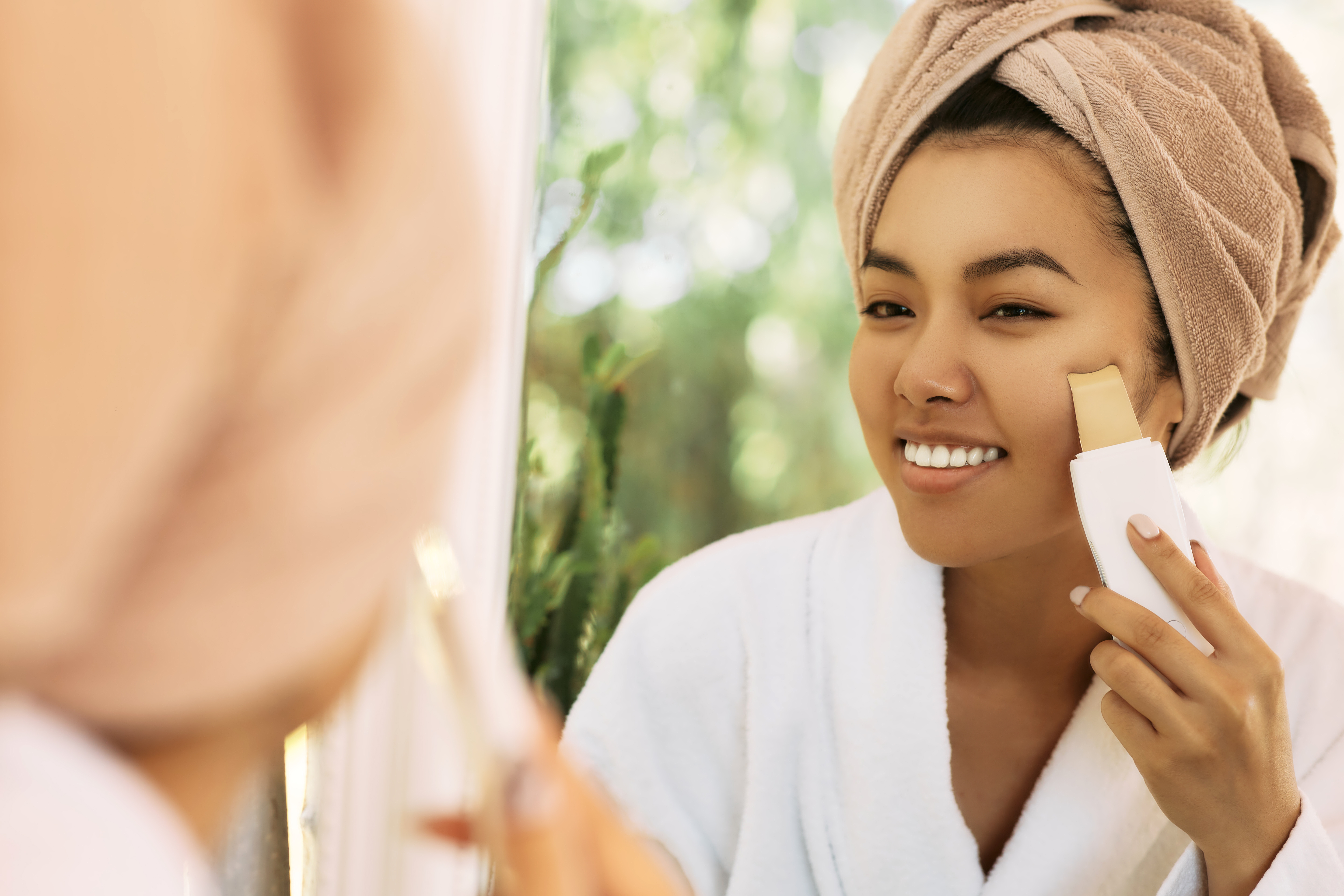 Cleansing facial skin, remove face blackheads. Asian woman looking at reflection in the mirror while ultrasonic peel skin procedure