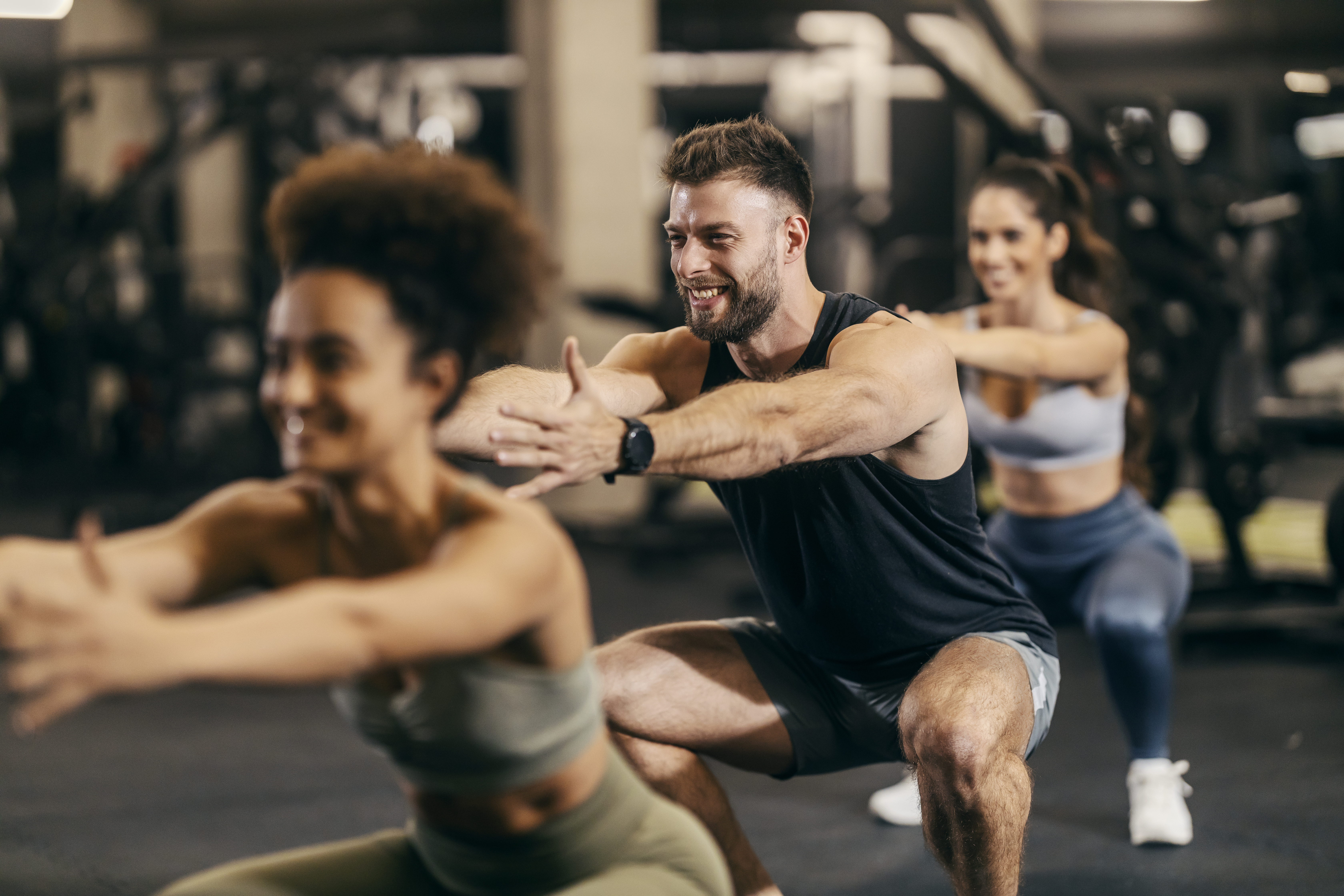Group of sporty friends doing squats with instructor in a gym.