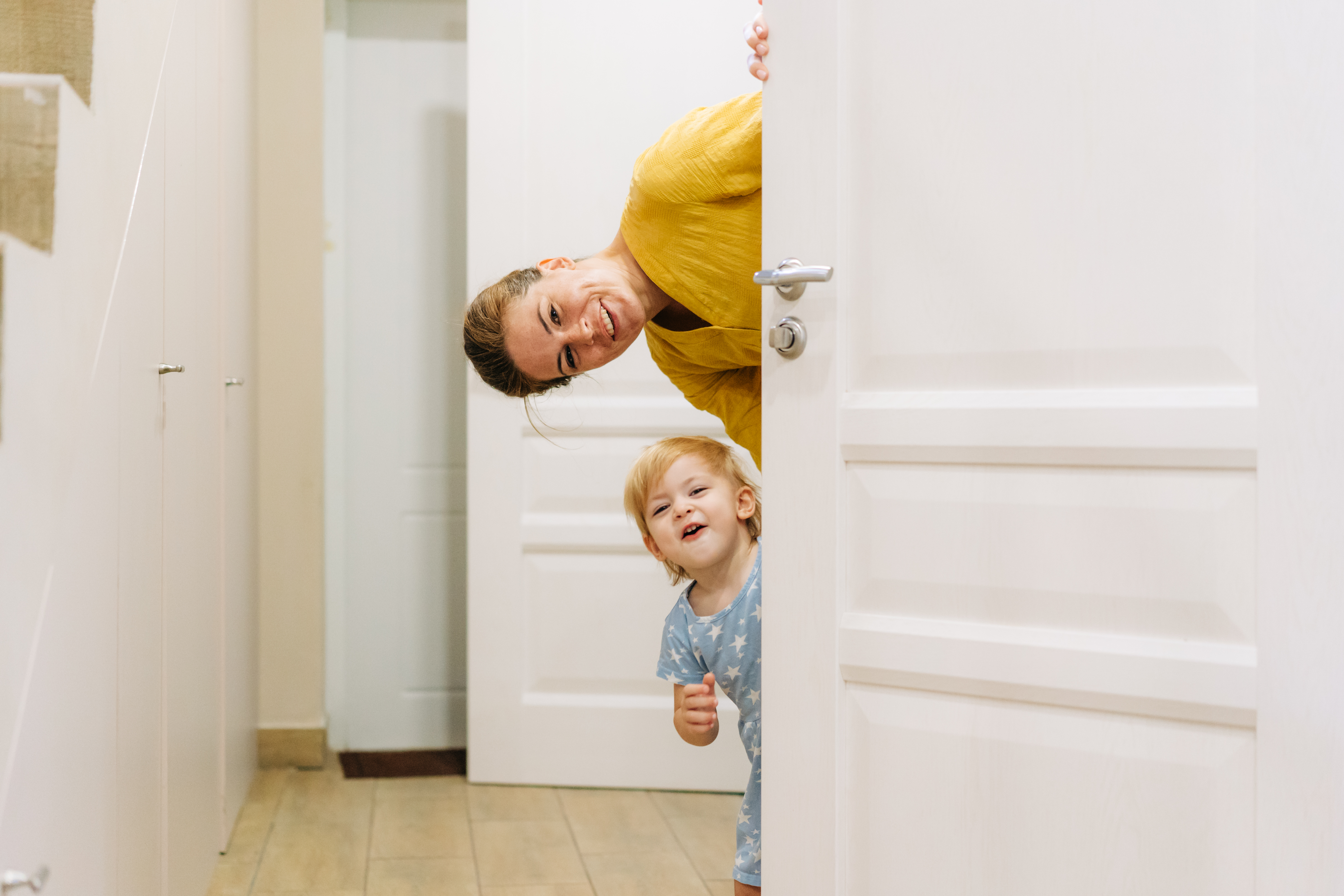 A young mother and little daughter play hide-and-seek behind the door of the house. A young mother and little daughter play hide-and-seek behind the door of the house.
