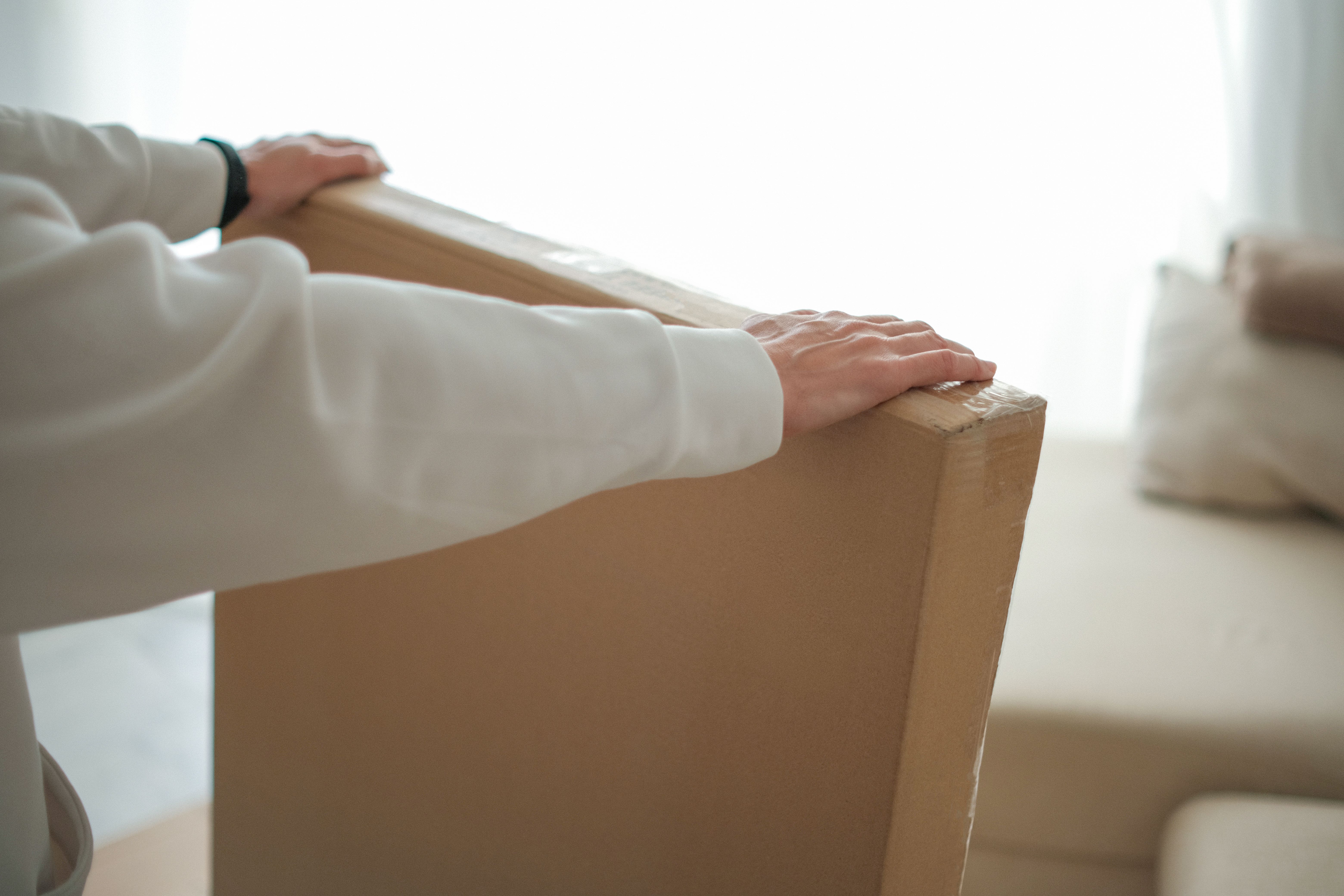 Woman hands holding large cardboard box with new furniture in bright, airy living room with sofa