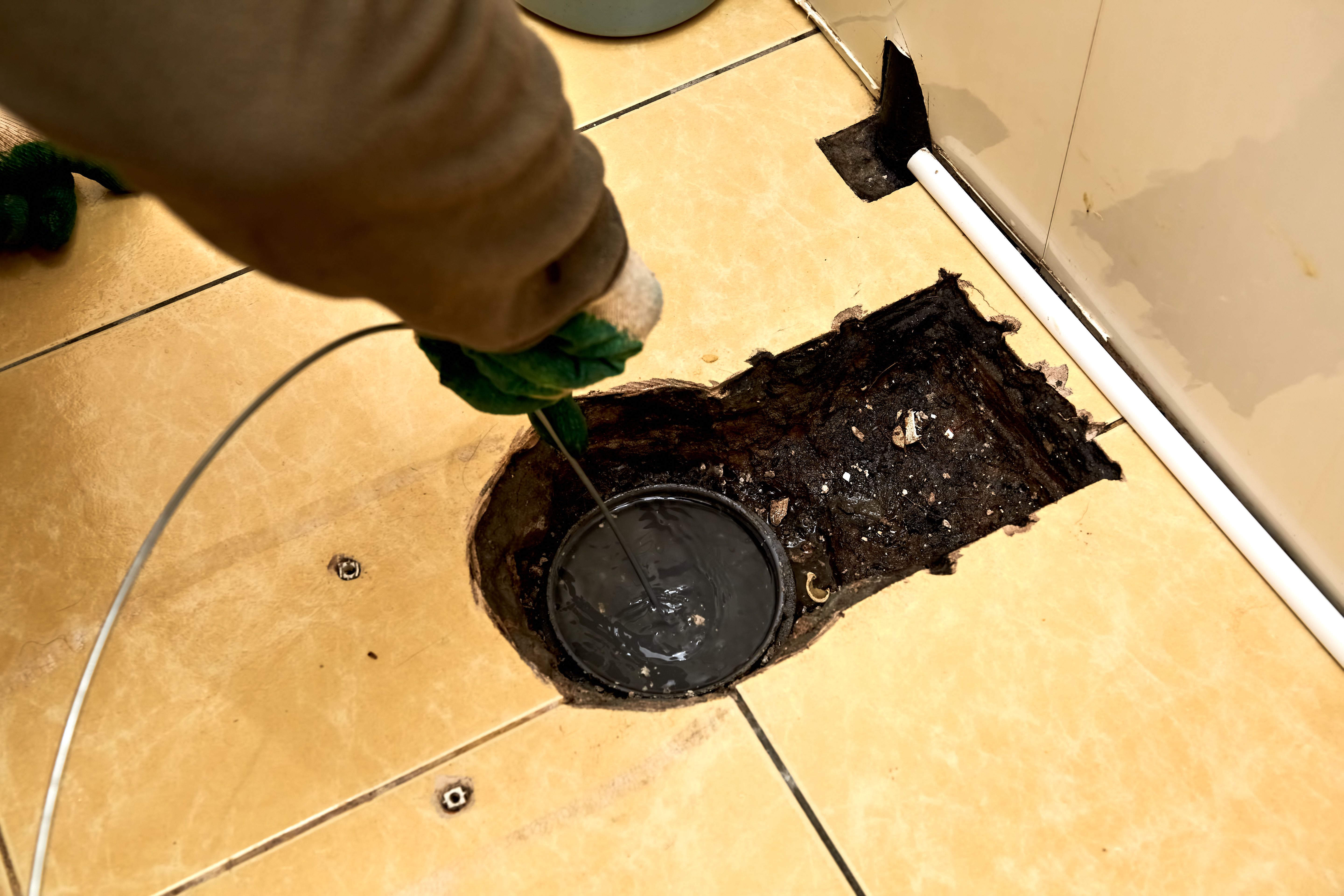 Sewer cleaning. A plumber uses sewer snake to clean blockage clog. Toilet room repair. Canalization pipe. Repairman hands. Bad smell. Dirty water. Metal wire. Yellow color tiles. Plumbing error. DIY