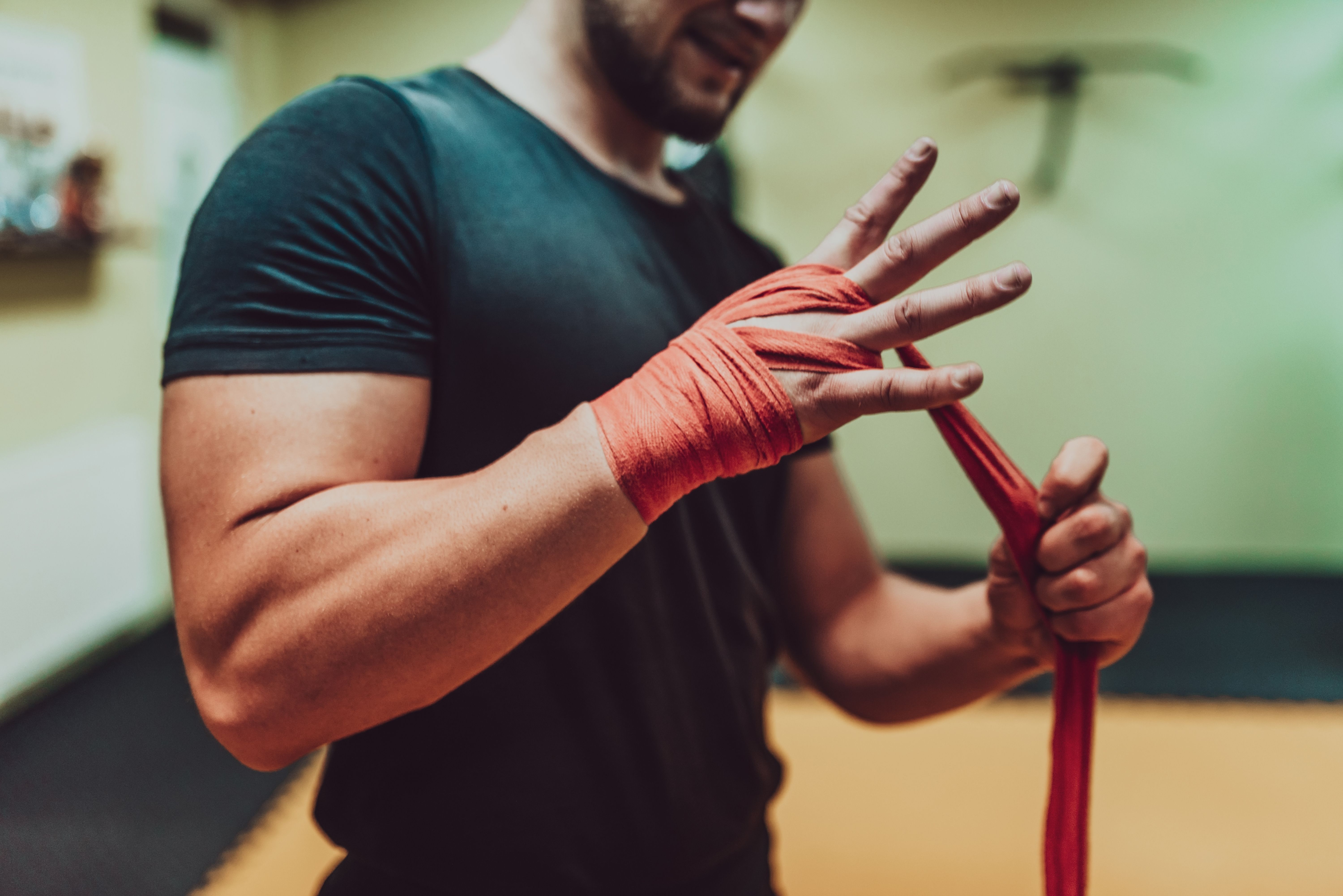 A male hand of boxer or fighter with red boxing bandages before the fight or training in sport gym.