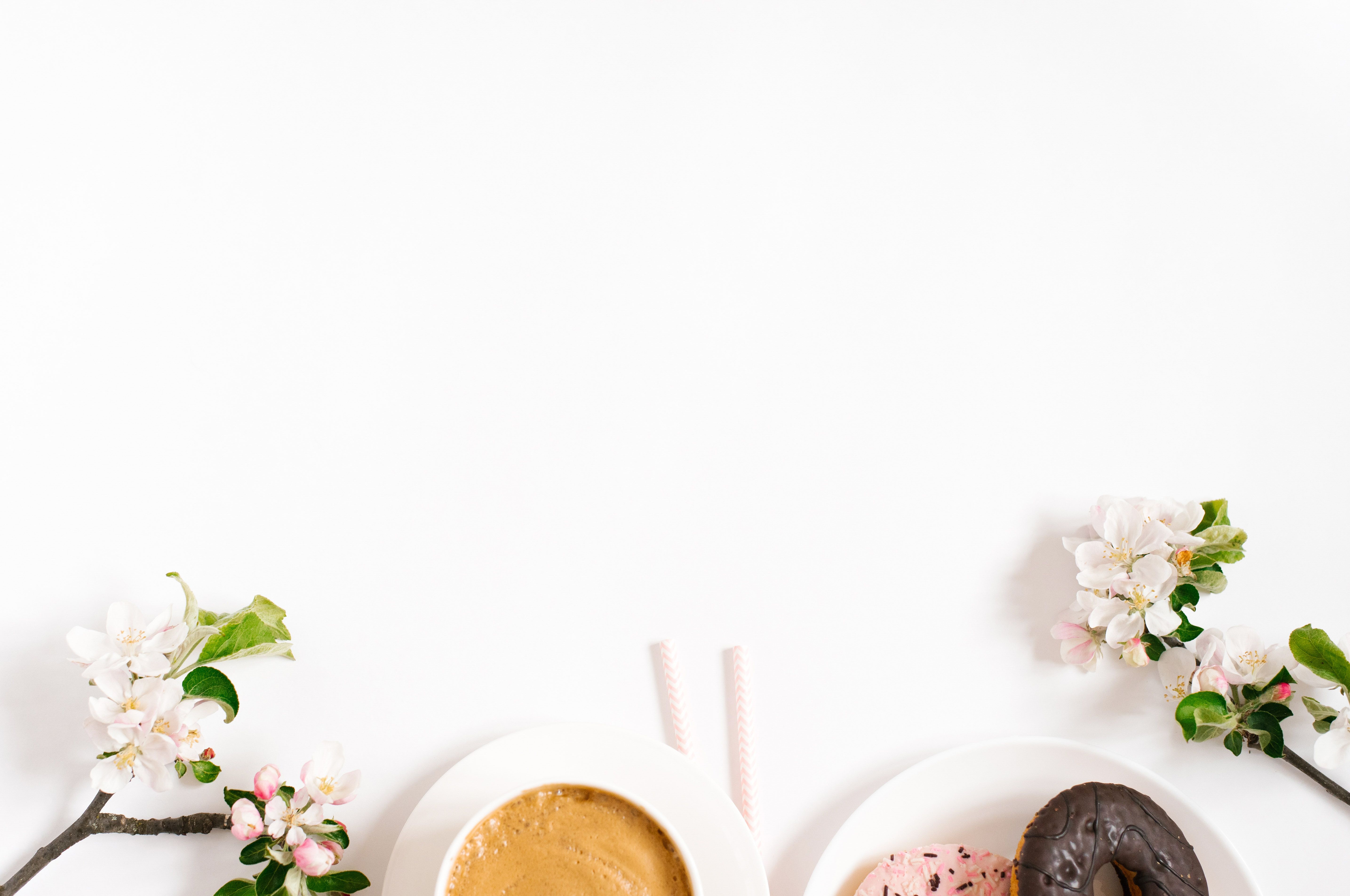 Stylish flat lay with cappuccino cup, apple blossoms, donuts on a white background with space copying. Morning breakfast or coffee break