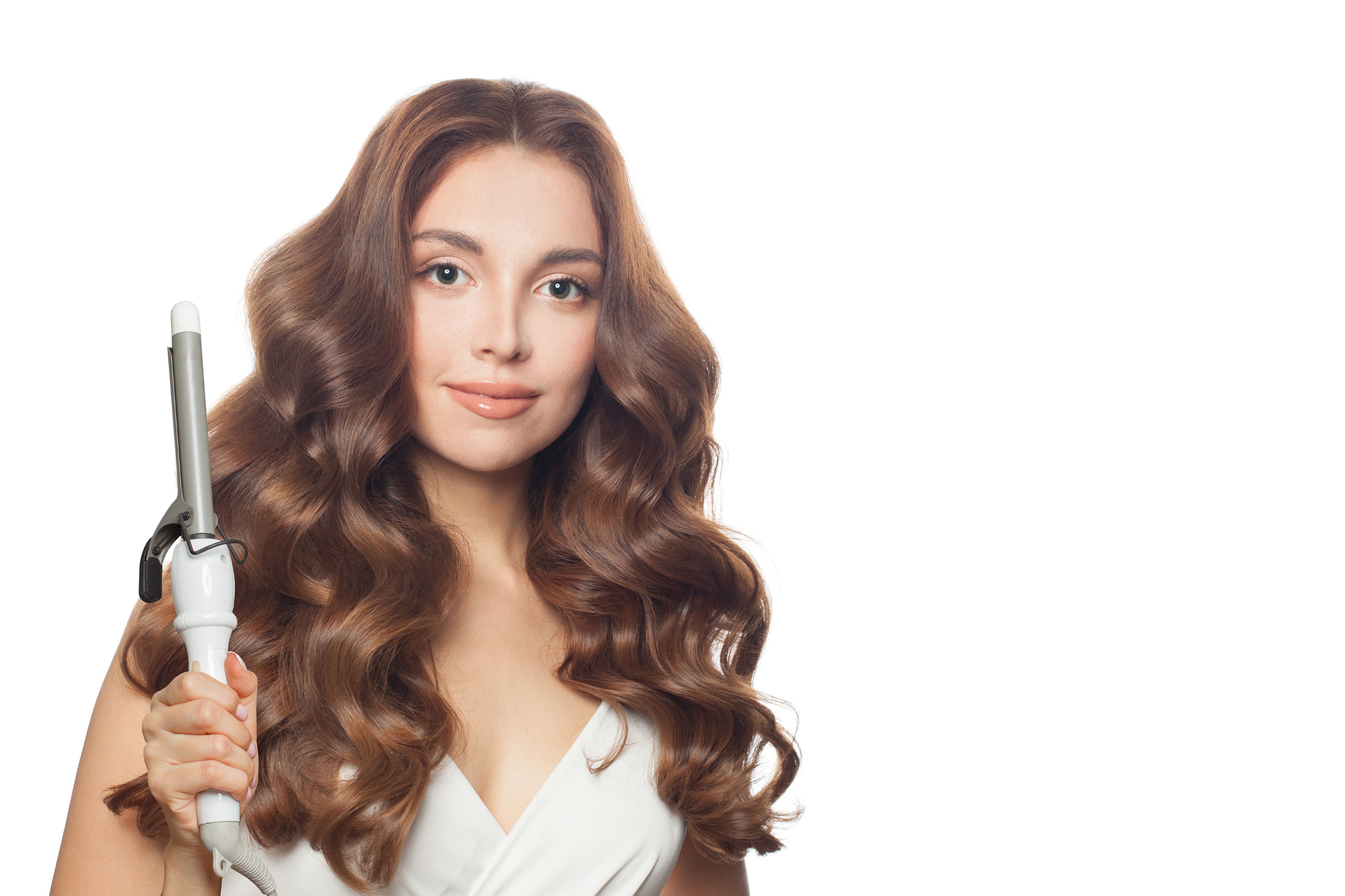 Fashionable  brunette model using curling iron on white background. Coiffure, beauty salon and hair styling concept