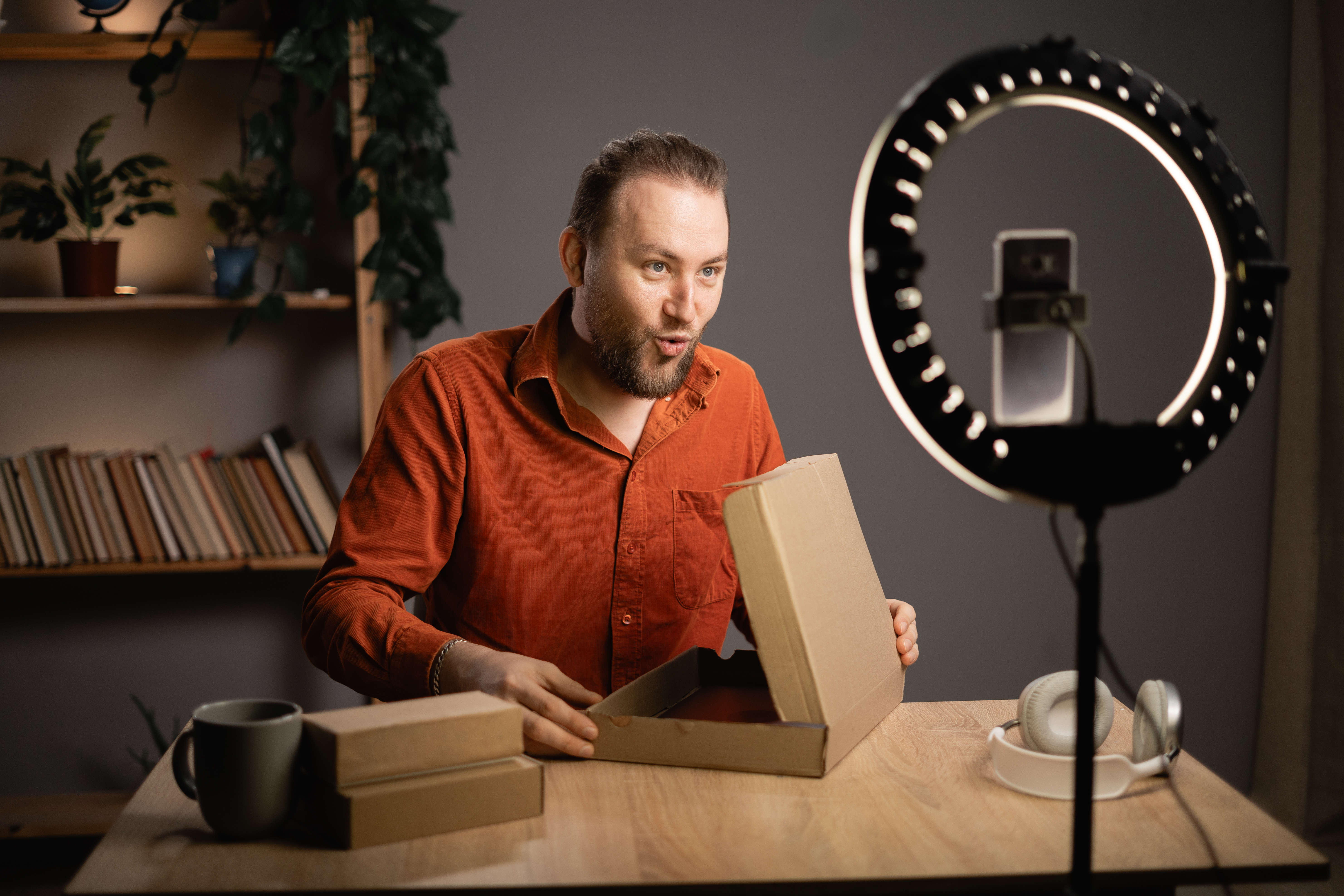 Male influencer unboxing a product and shooting video for social media sitting in authentic home interior.